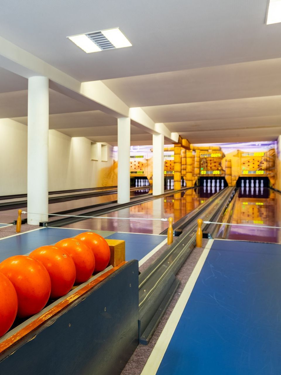 Bowlingbahn mit orangefarbenen Bowlingkugeln im Vordergrund, Bahnen und dekorativer Wüstenkulisse.