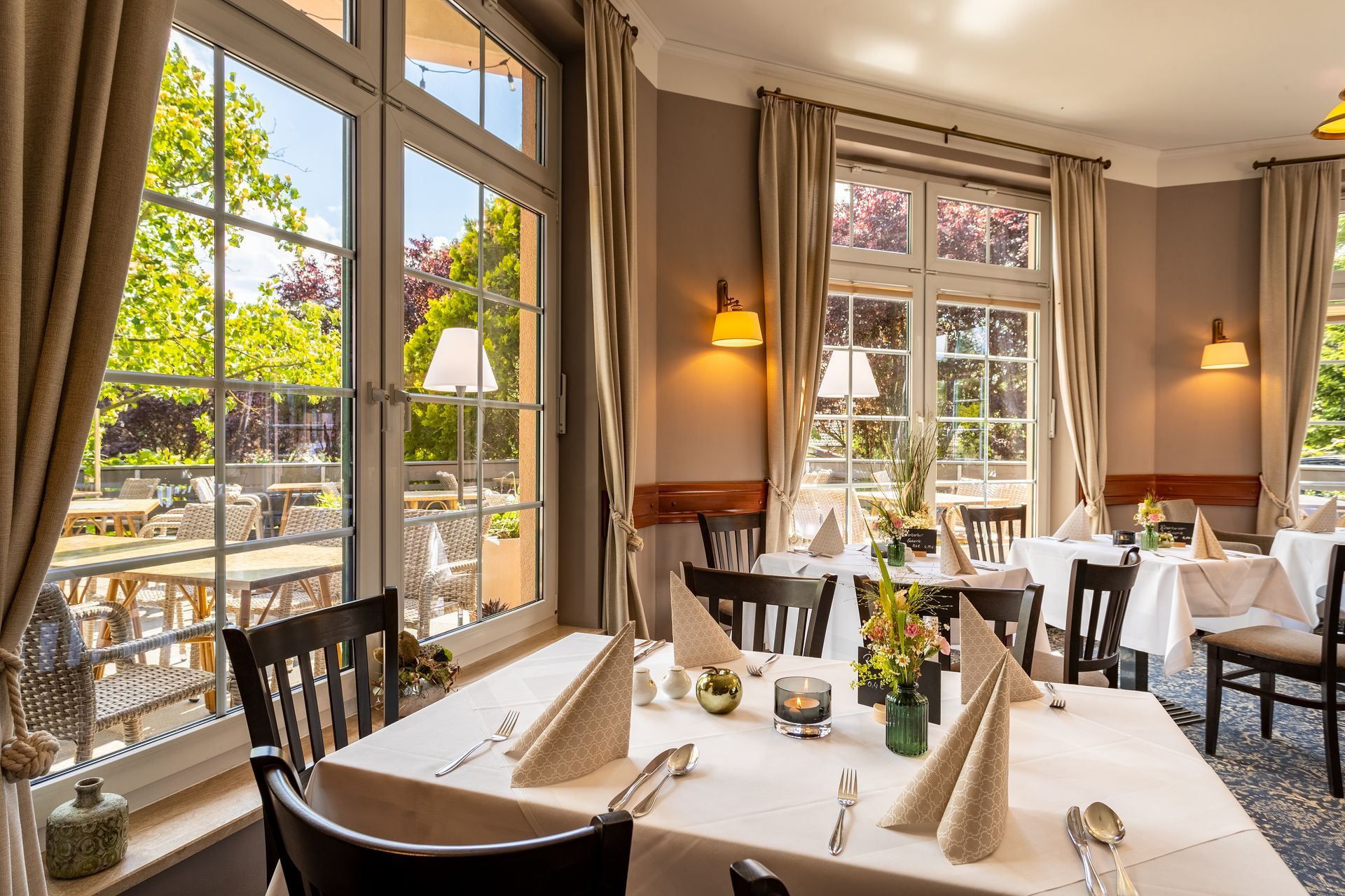 Inneneinrichtung des Restaurants mit Tischen an großen Fenstern mit Blick auf eine Terrasse.