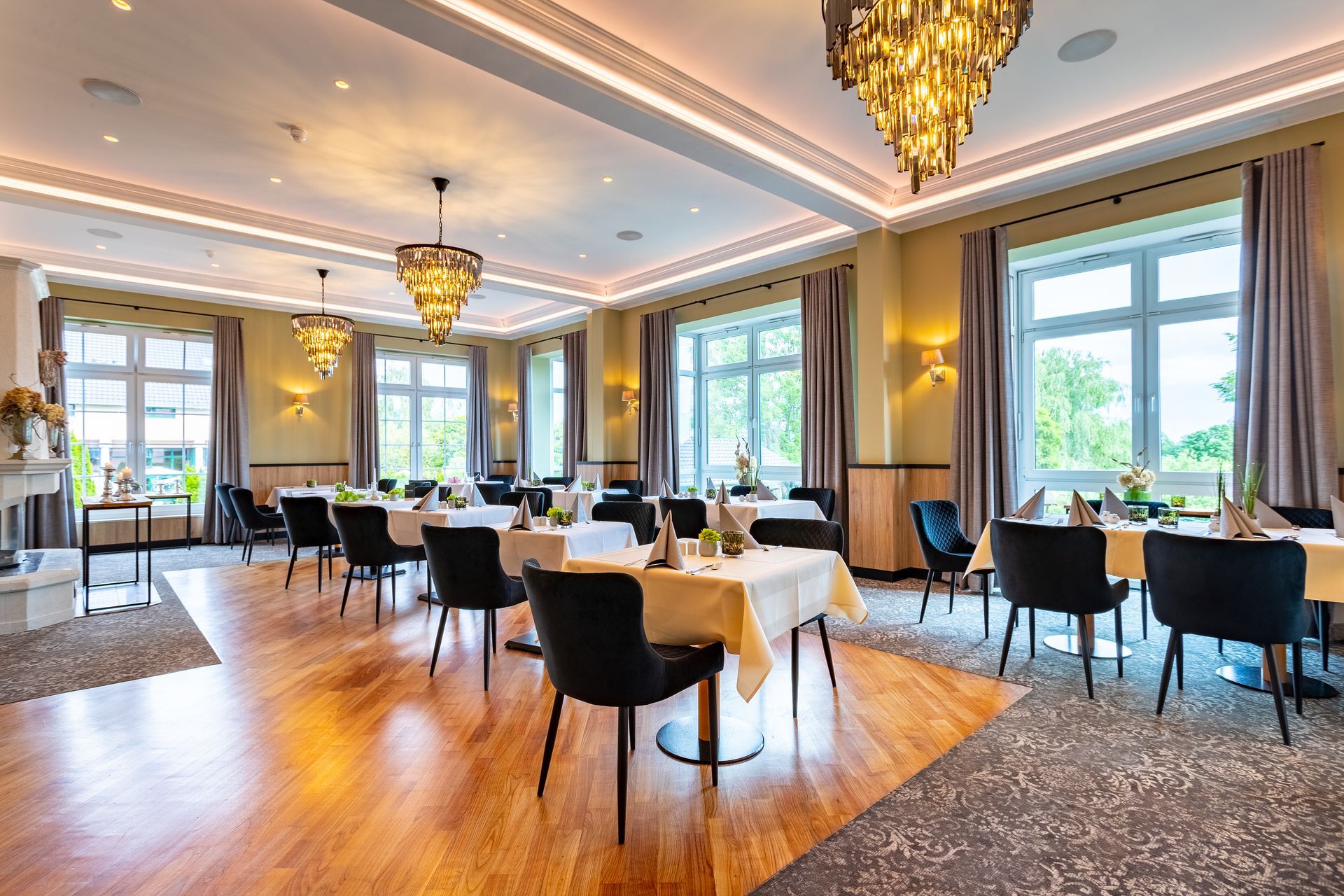 Eleganter Speisesaal des Restaurants mit gedeckten Tischen, goldenen Kronleuchtern und großen Fenstern.