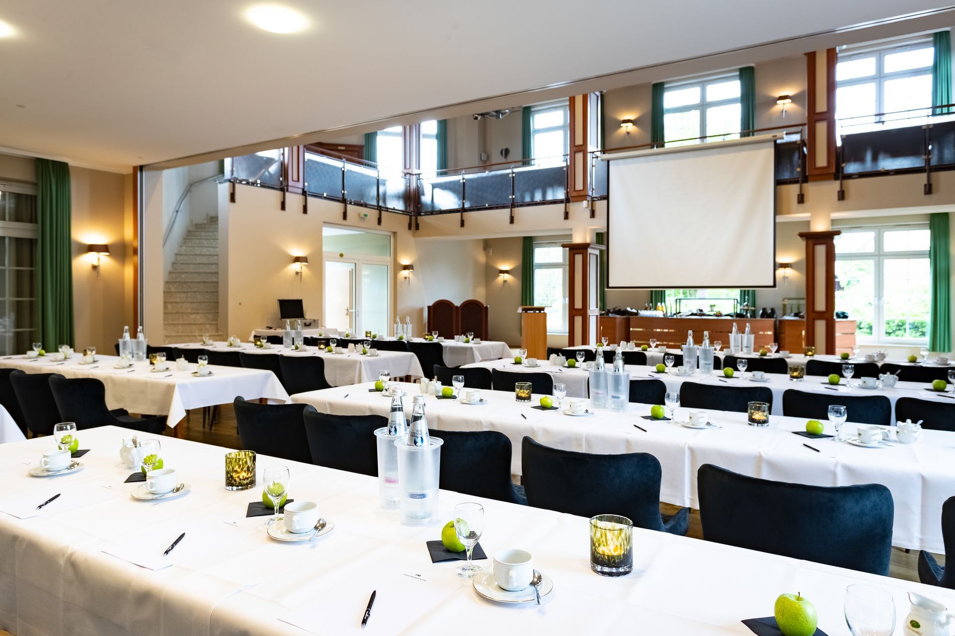Für eine Veranstaltung eingerichteter Konferenzraum mit Reihen von Tischen und einer Projektionsleinwand.
