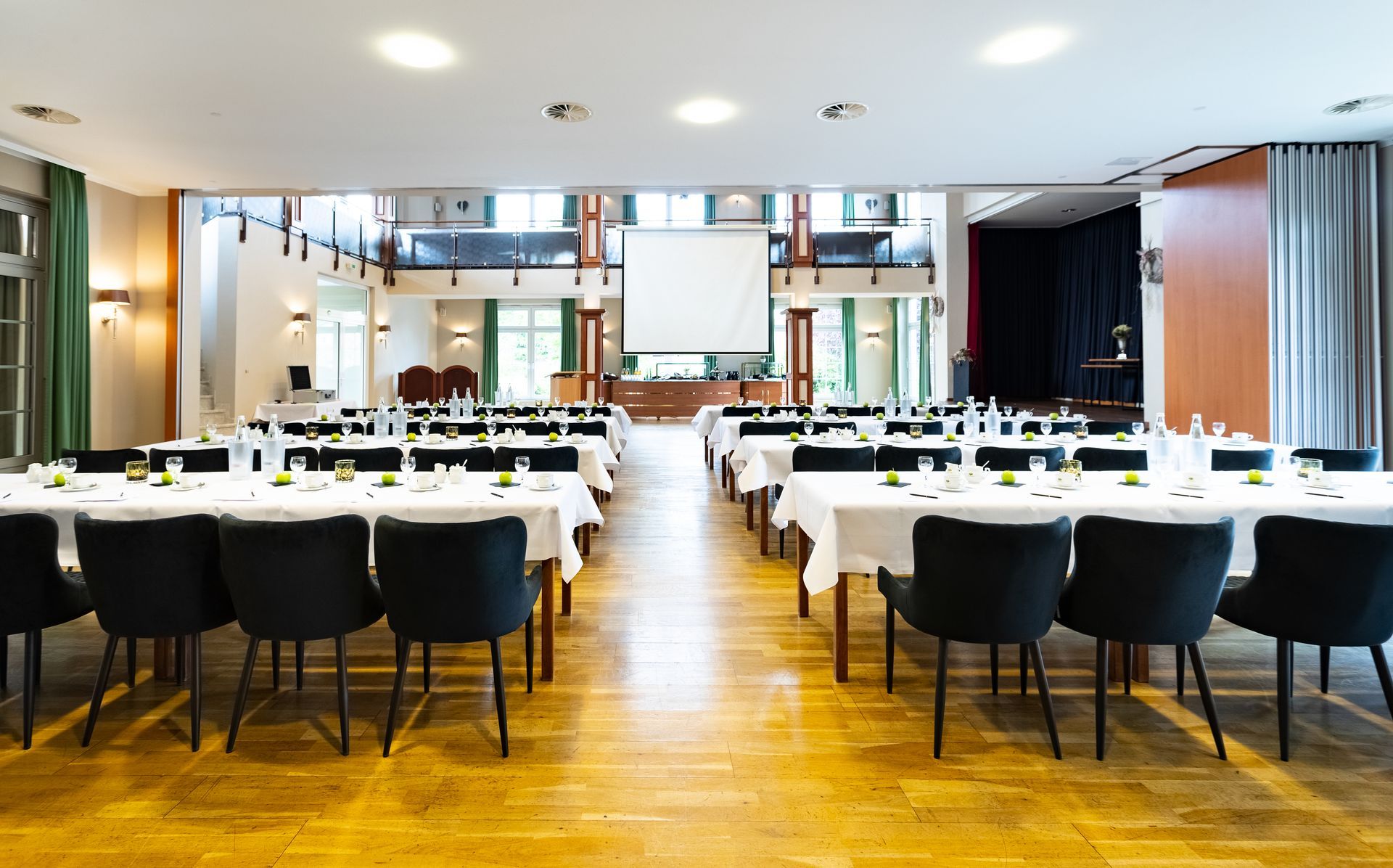 Formeller Veranstaltungsraum mit rechteckigen Tischen für eine Versammlung. Weiße Tischdecken, schwarze Stühl