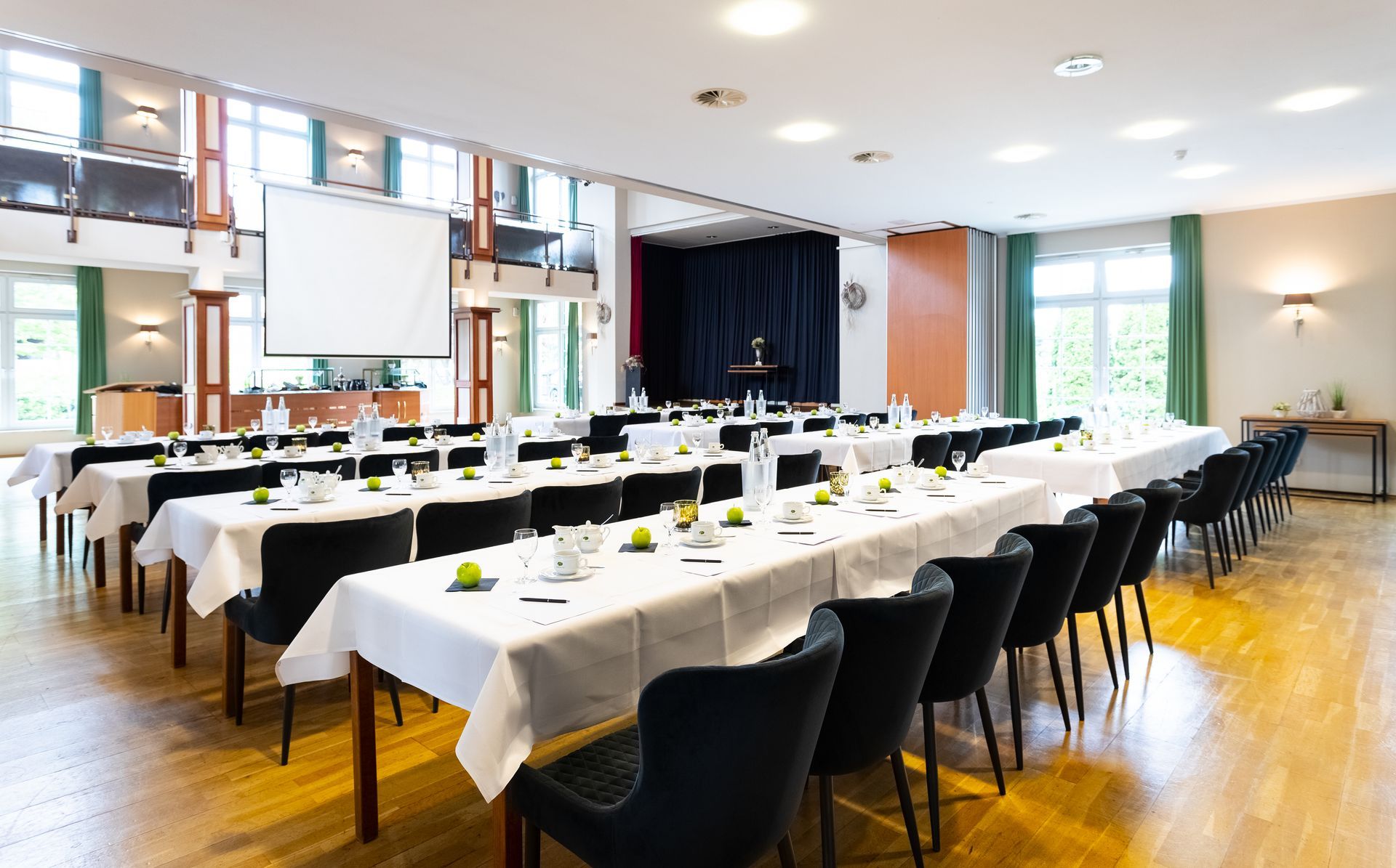 Konferenzraum mit langen, für eine Besprechung gedeckten Tischen, schwarzen Stühlen und einer Bühne im Hintergrund.
