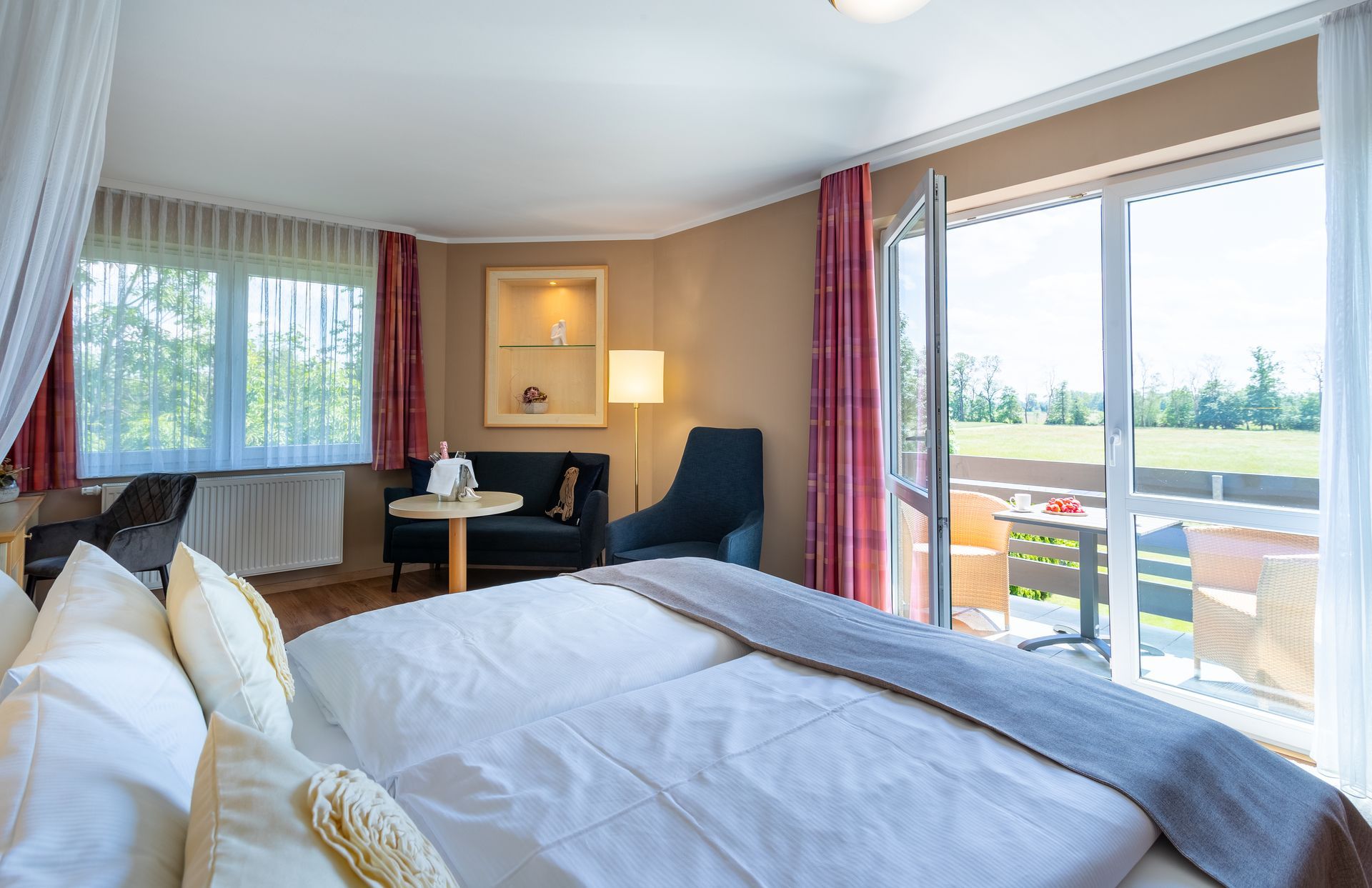 Schlafzimmer mit Doppelbett, kleinem Tisch, Sofa und offenen Glastüren, die auf eine Terrasse führen.