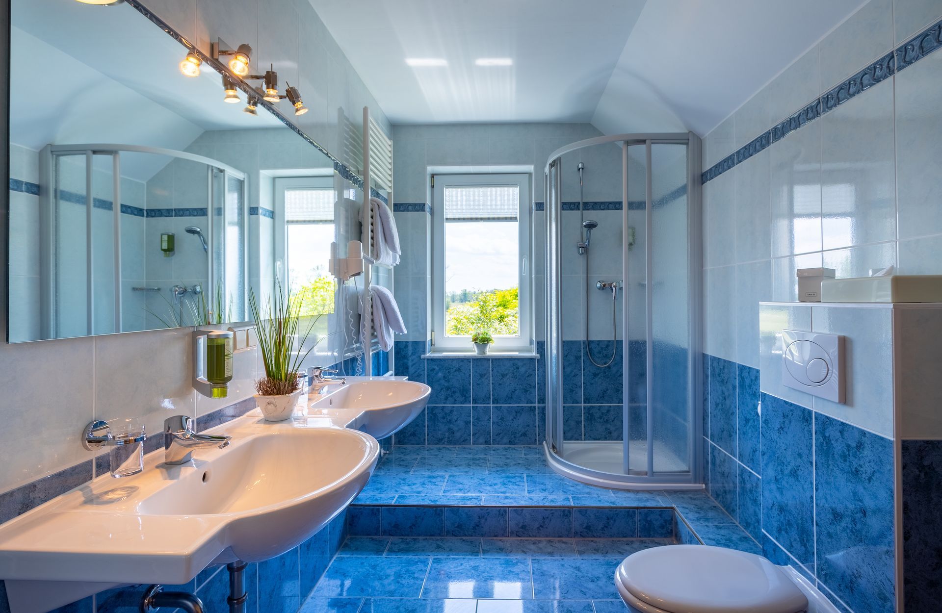 Blau-weißes Badezimmer mit zwei Waschbecken, einer Dusche und einem Fenster mit Aussicht.