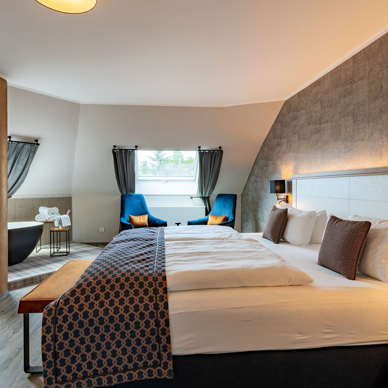 Hotelzimmer mit einem großen Bett, zwei blauen Stühlen und einer Badewanne.