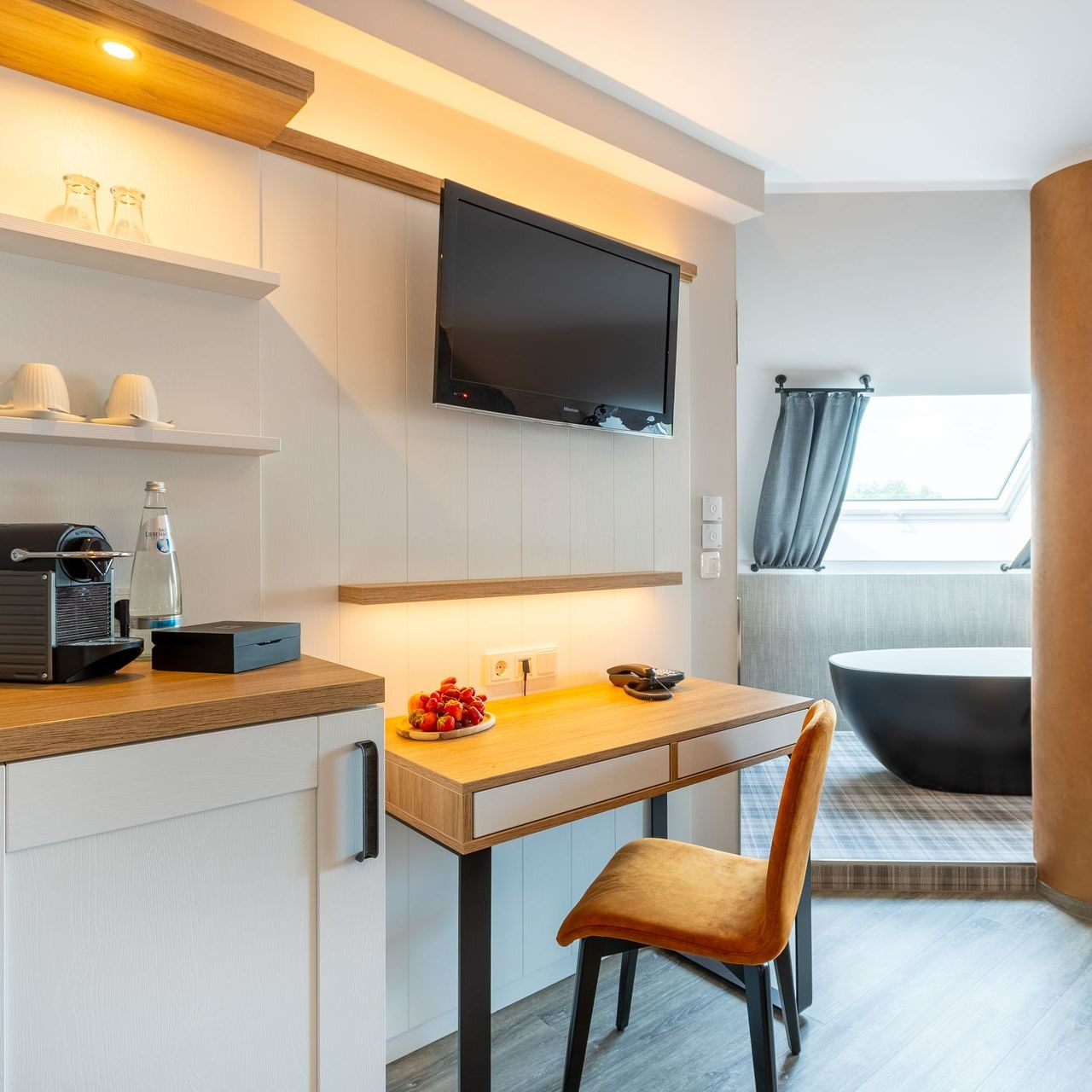 Hotelzimmer mit Schreibtisch, Fernseher und schwarzer Badewanne.