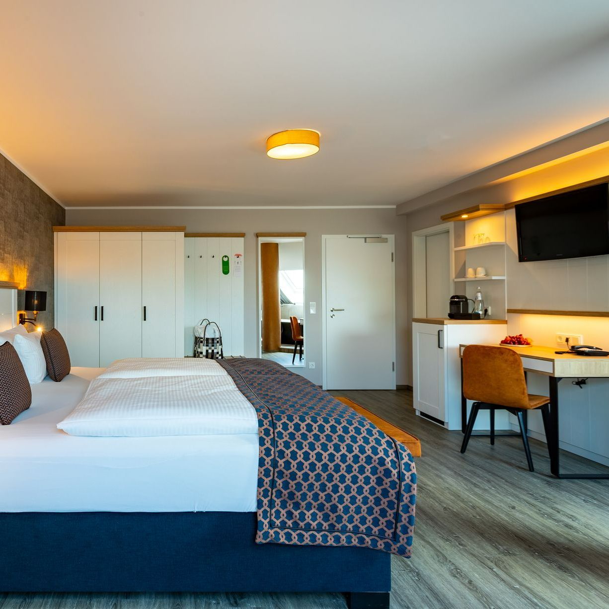 Schlafzimmer mit Bett, Schreibtisch und Kleiderschrank. Neutrale Farben mit einem Hauch von Blau und Orange.