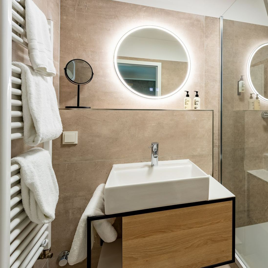 Badezimmer mit weißem Waschbecken, hinterleuchtetem Spiegel und Handtuchwärmer. Beige Wände.