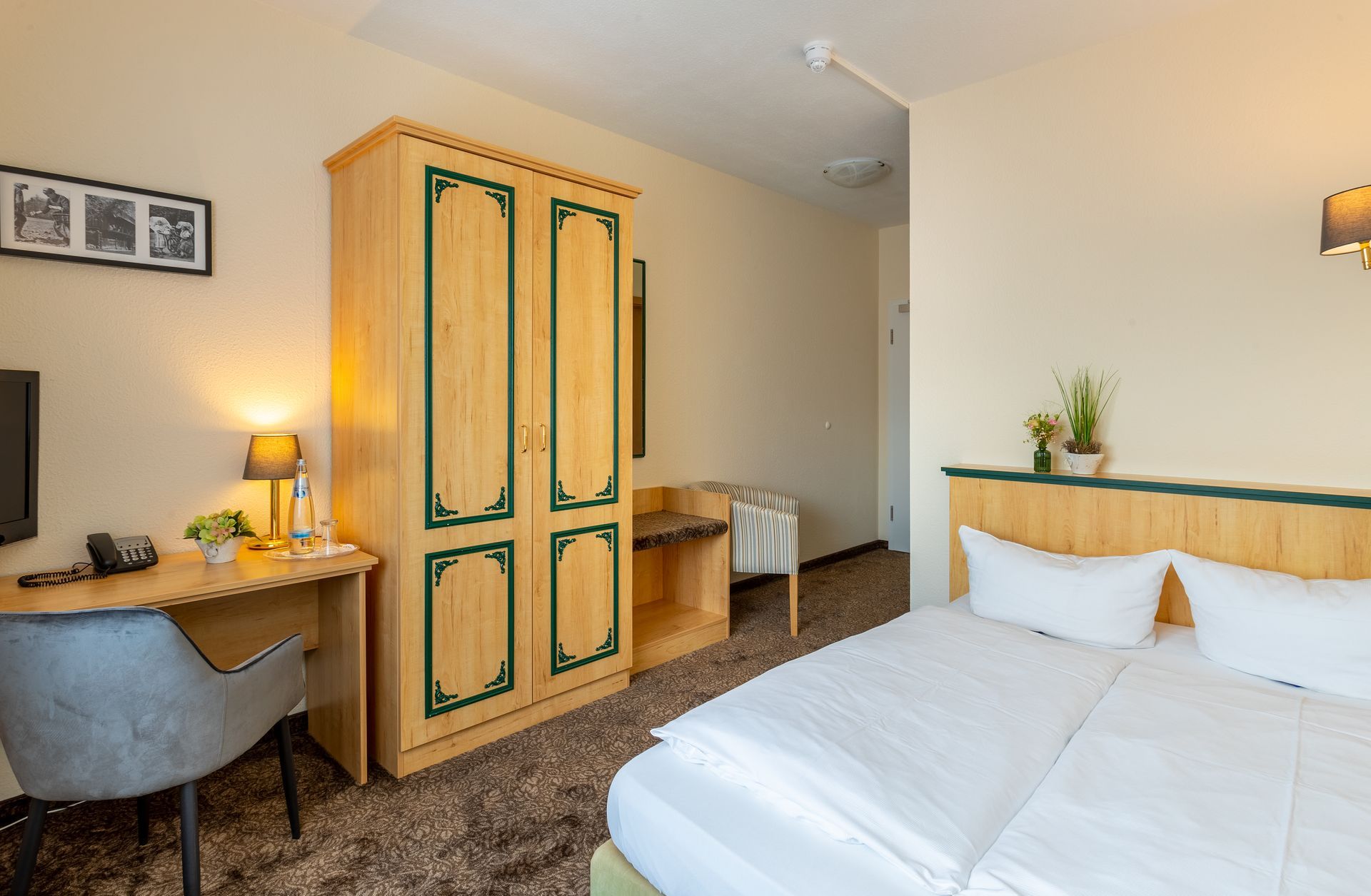 Hotelzimmer mit Bett, Holzschrank, Schreibtisch und Stuhl.
