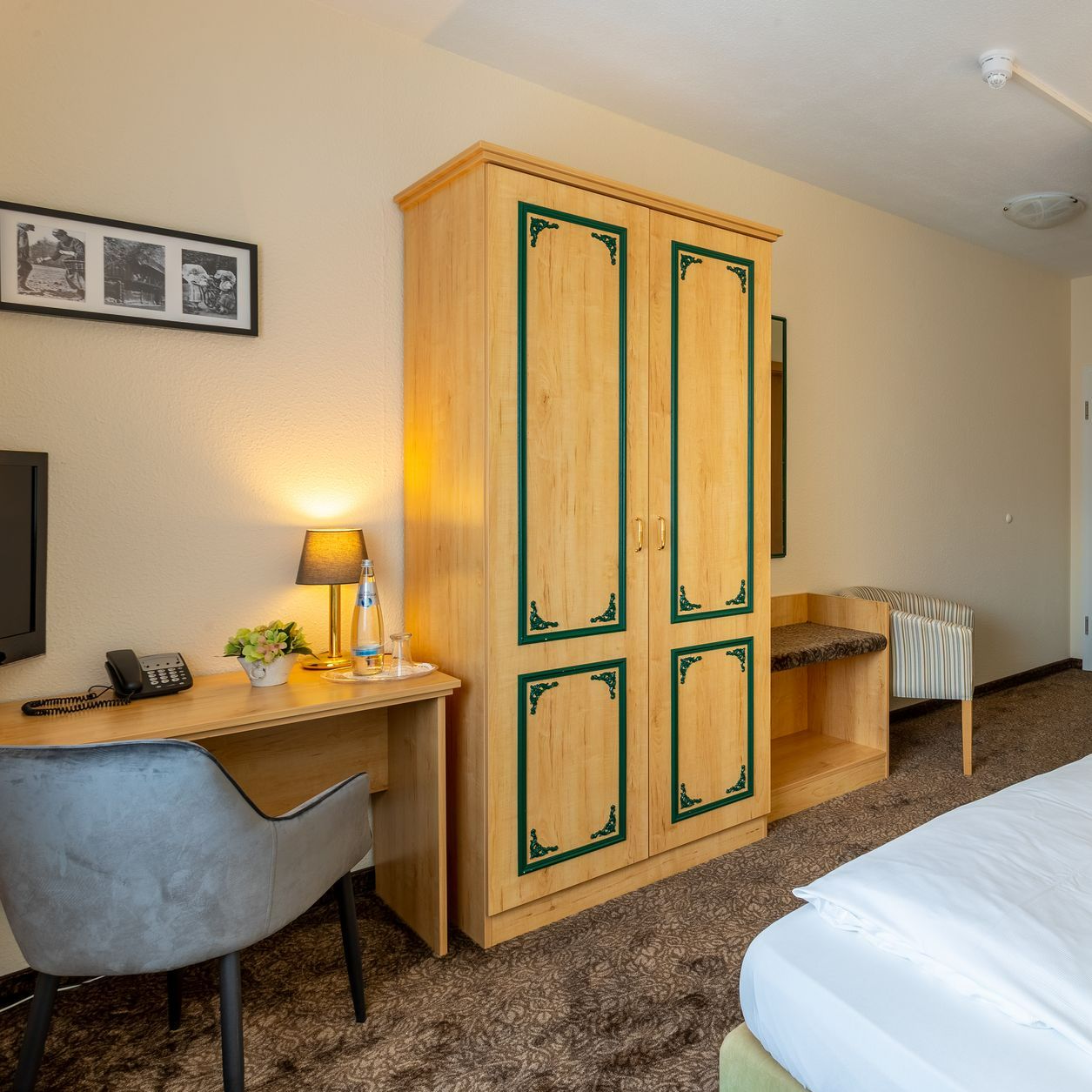 Hotelzimmer mit Holzschrank, Schreibtisch, Stuhl und Bett.