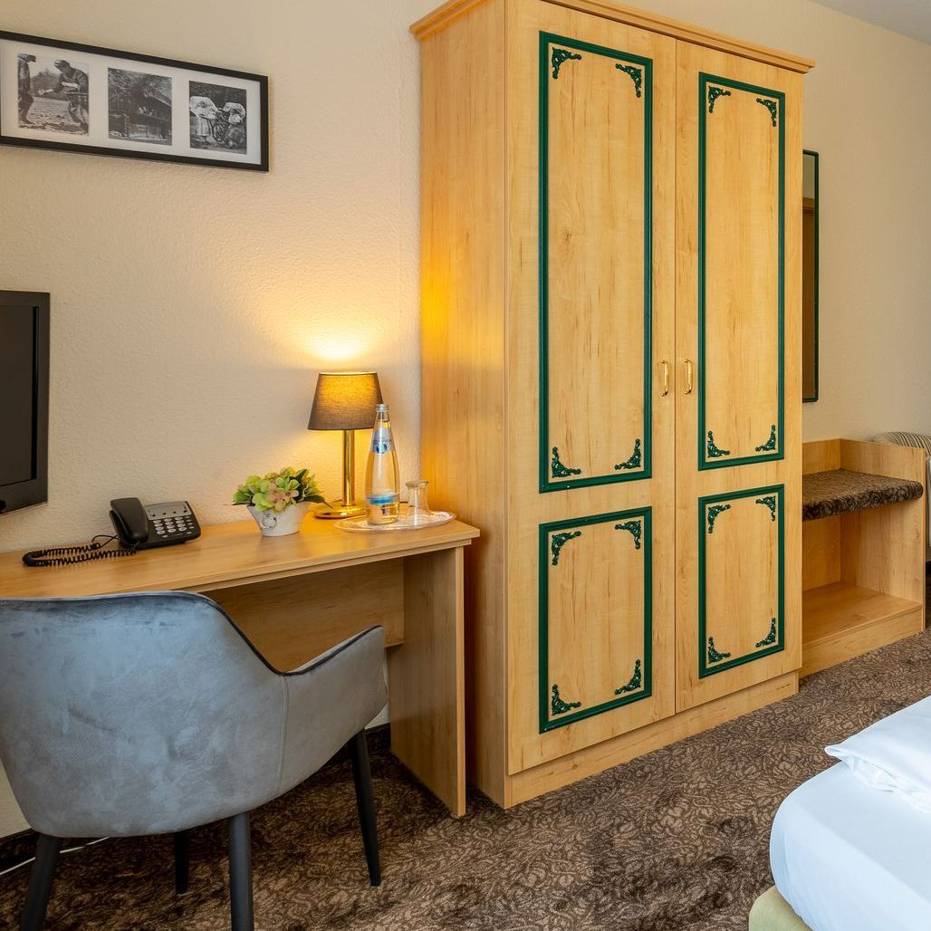 Ein Hotelzimmer mit Holzschrank, Schreibtisch, Stuhl und Bett.