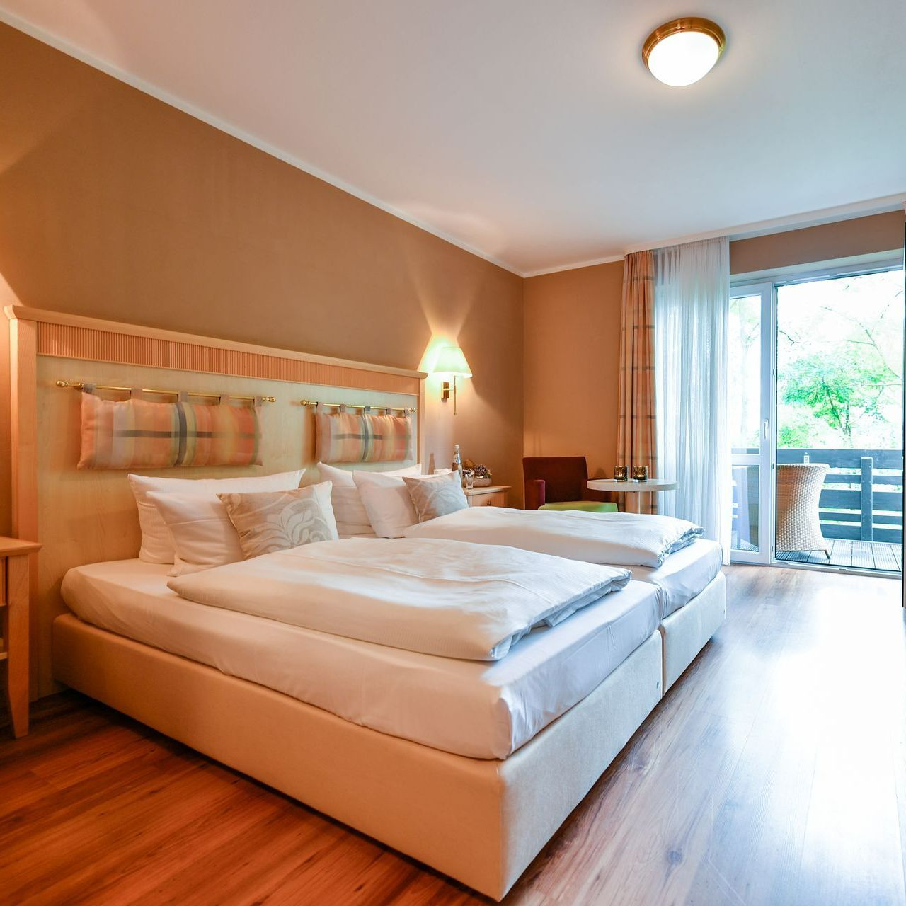 Ein Hotelzimmer mit Doppelbett, Balkon und Wänden und Böden in warmen Farbtönen.