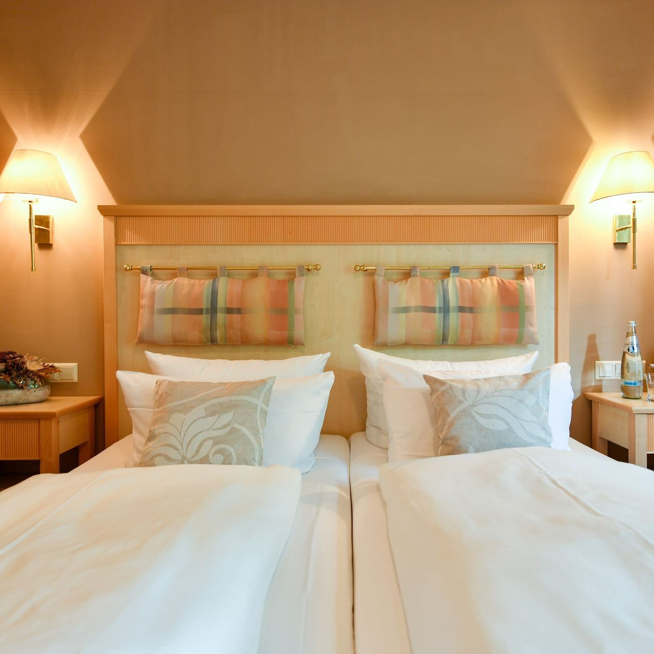 Zwei Einzelbetten mit weißer Bettwäsche, dekorativen Kissen und Kunstwerken am Kopfteil.