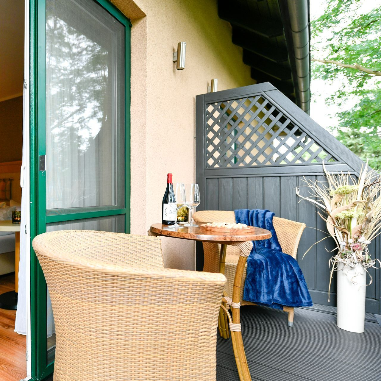 Gemütlicher Balkon mit Korbmöbeln, einem Tisch mit Wein und einer blauen Decke.