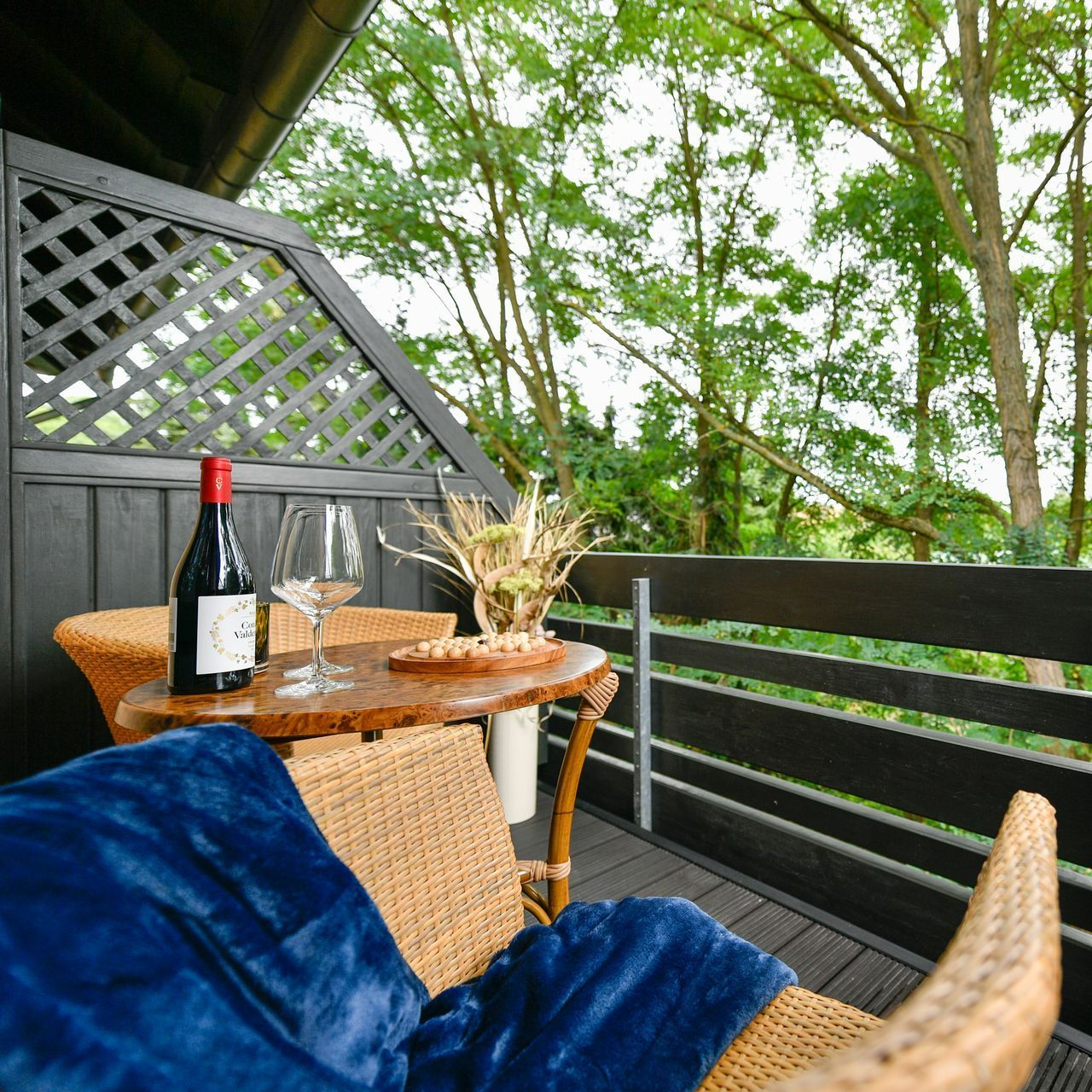 Gemütlicher Balkon mit Wein, Gläsern und Snacks auf einem Tisch und Blick auf einen üppigen Wald.
