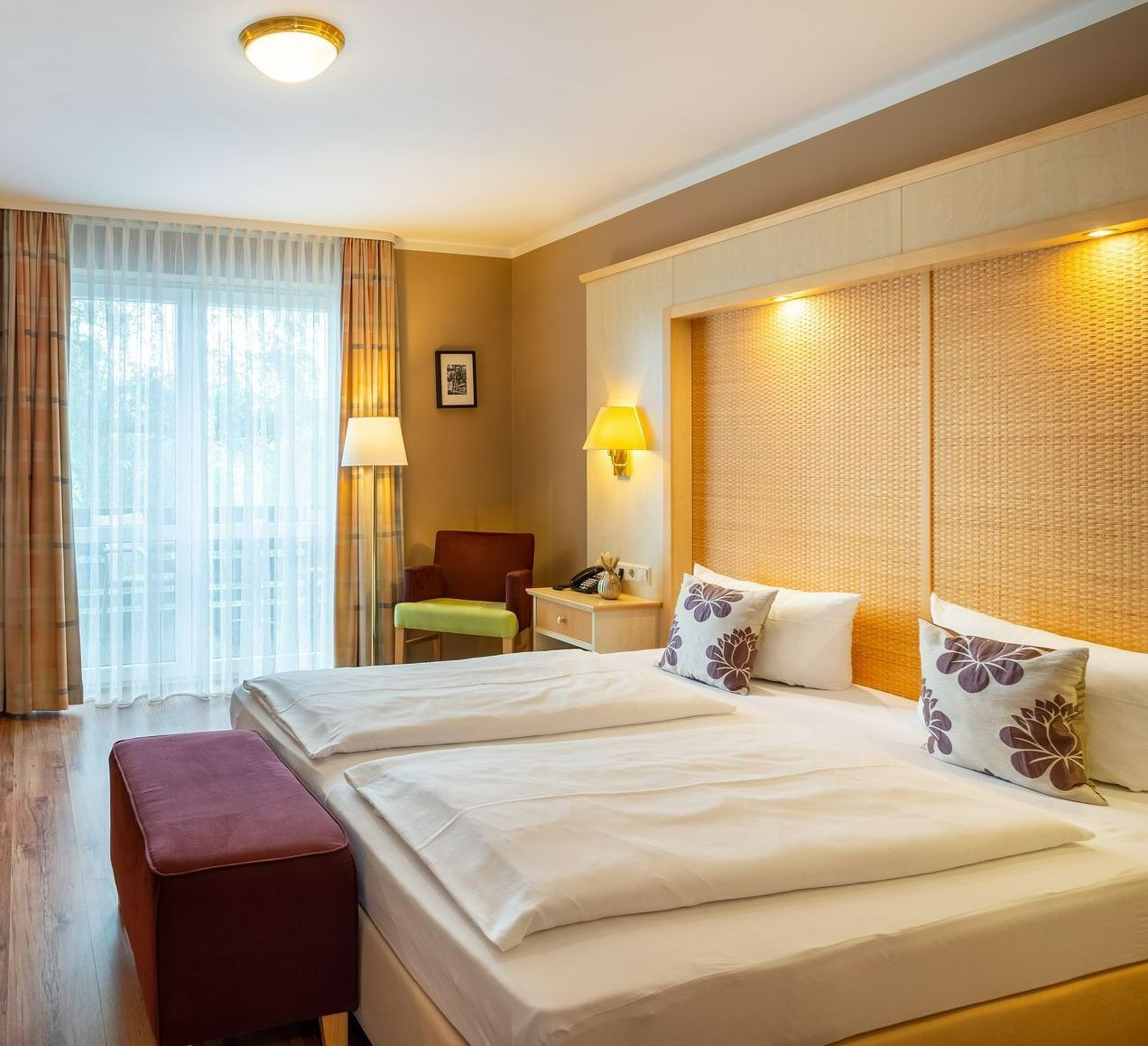 Hotelschlafzimmer mit Doppelbett, Zugang zum Balkon, warmen Farbtönen und dekorativen Kissen.