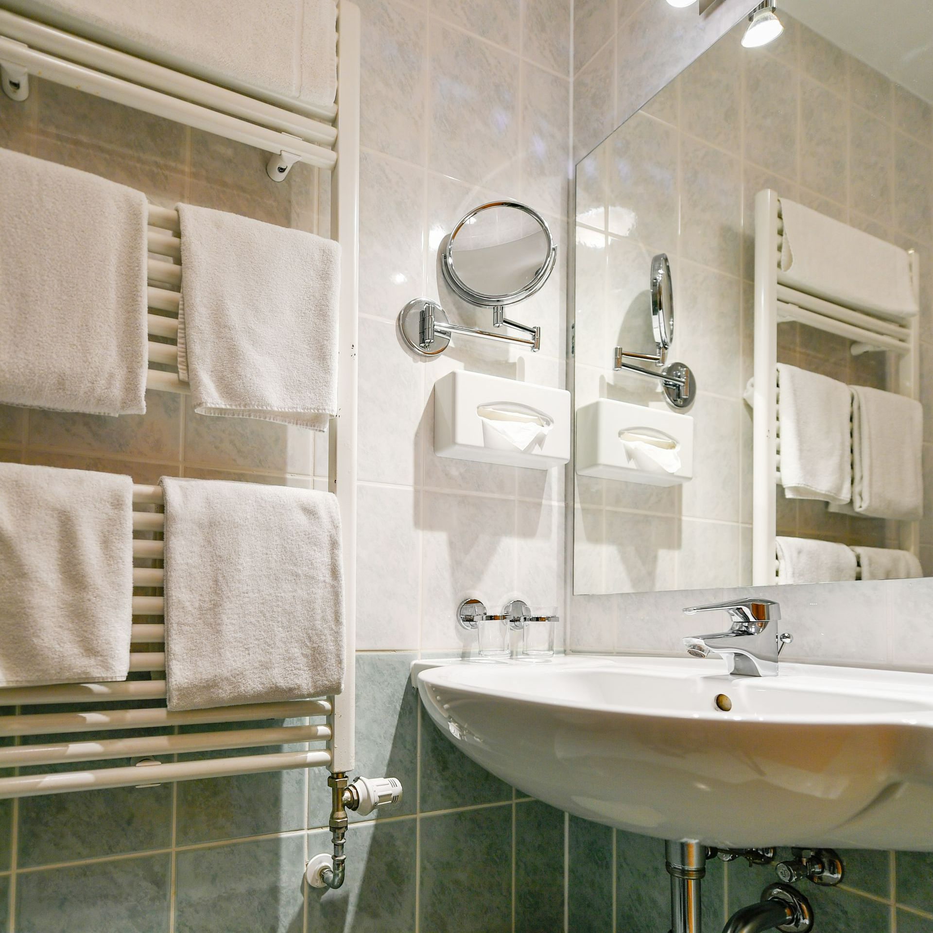 Badezimmer mit weißen Handtüchern auf einem beheizten Ständer, weißem Waschbecken und Spiegel.