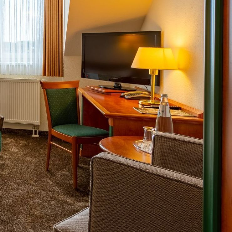 Hotelzimmer mit Schreibtisch, Fernseher, Lampe, Stuhl, Sofa und Fenster.