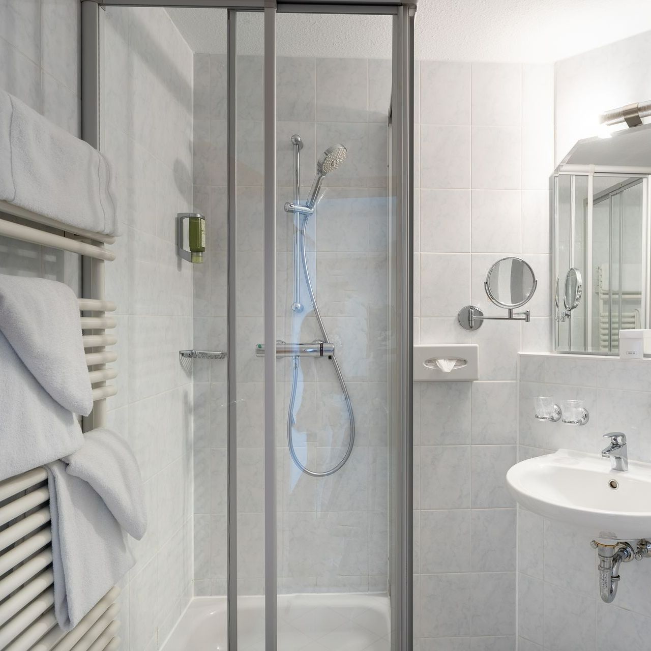 Kleines, weißes Badezimmer mit Dusche, Waschbecken und Handtuchhalter.