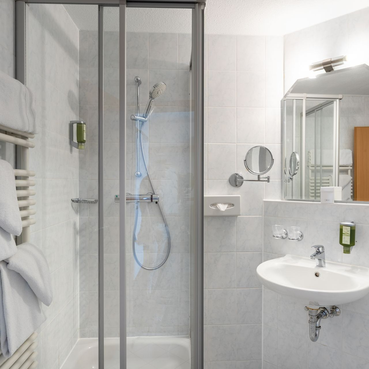 Badezimmer mit Dusche, Waschbecken, Spiegel und weißen Handtüchern auf einem Ständer.