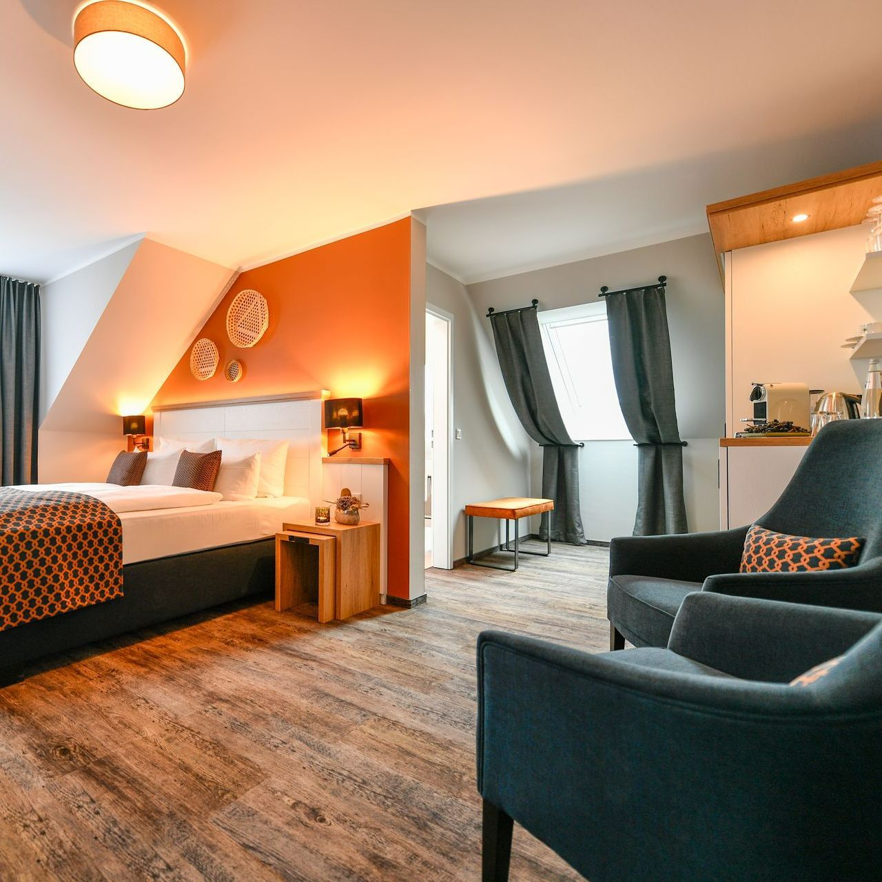 Hotelzimmer mit Bett, Sitzecke und orangefarbener Akzentwand.
