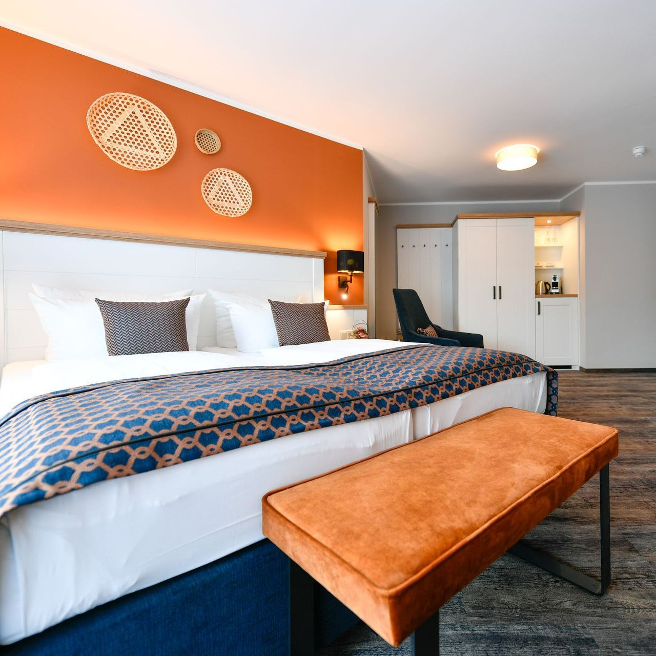 Hotelschlafzimmer mit Kingsize-Bett, orangefarbener Akzentwand und Bank.