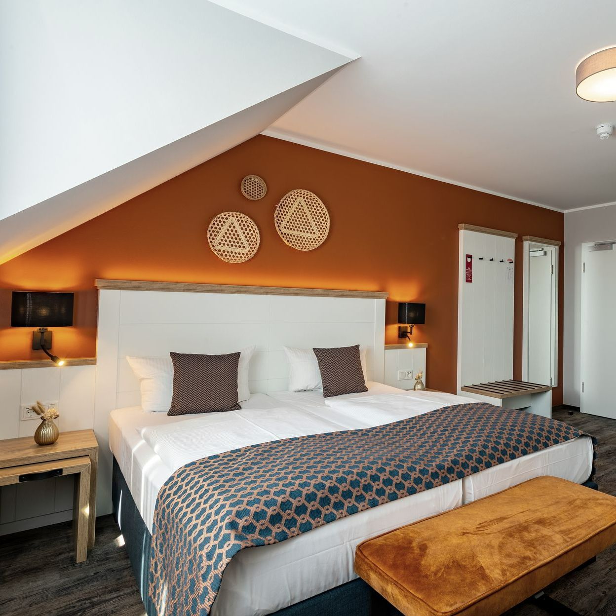 Hotelschlafzimmer mit Kingsize-Bett, orangefarbener Akzentwand und Holzdekor.