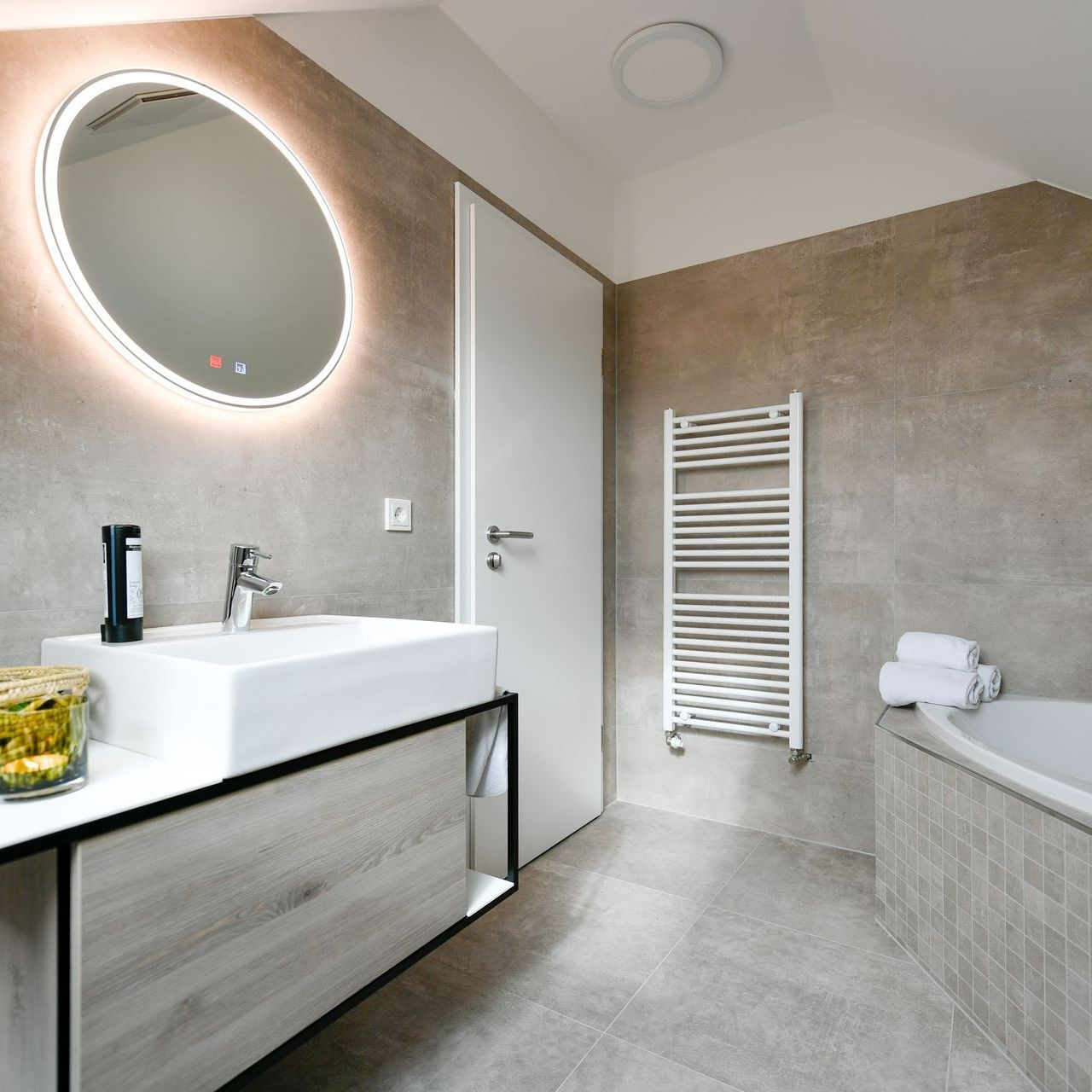 Modernes Badezimmer mit hinterleuchtetem Spiegel, weißem Waschbecken, Handtuchwärmer und Badewanne.