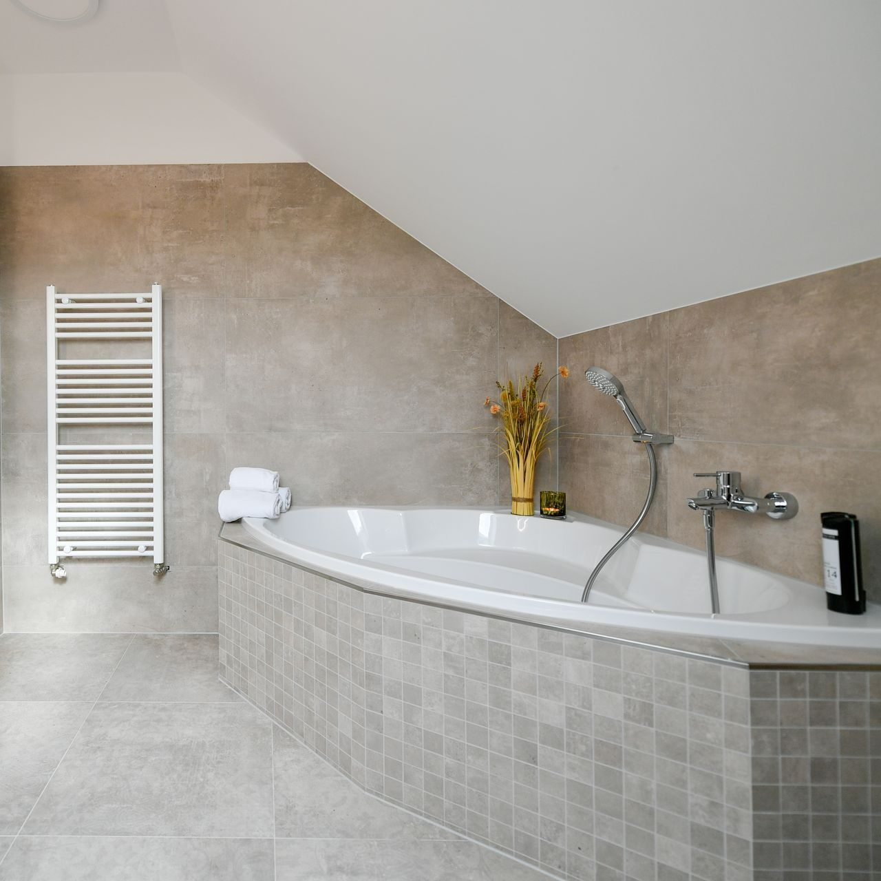 Badezimmer mit weißer Badewanne, hellgrauen Fliesen und Heizkörper.