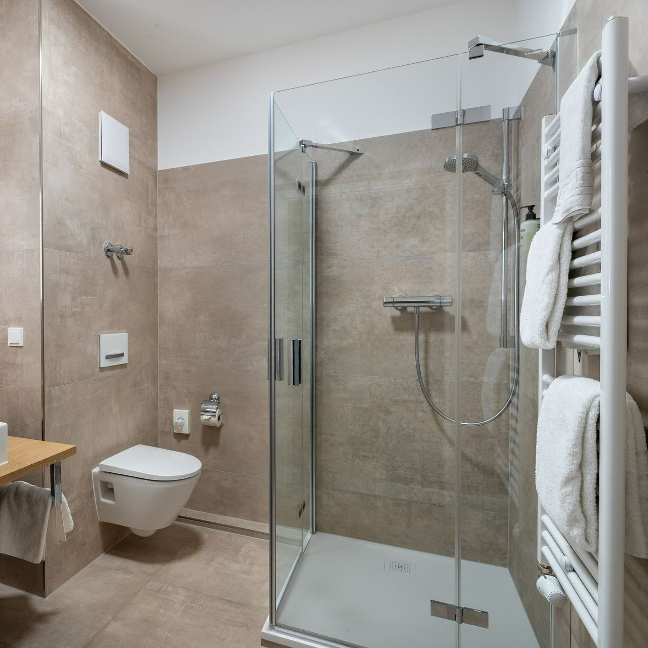 Modernes Badezimmer mit ebenerdiger Dusche, Toilette und Handtuchhalter. Beige geflieste Wände und Boden.