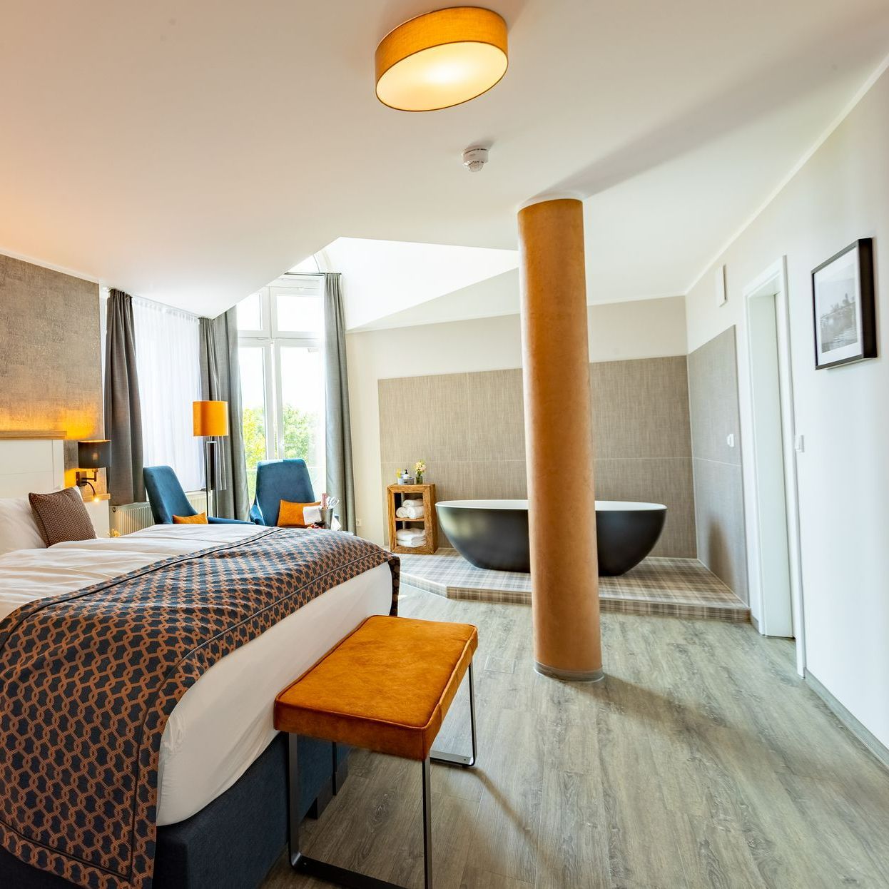 Hotelzimmer mit Bett, Badewanne und orangefarbenen Akzenten.
