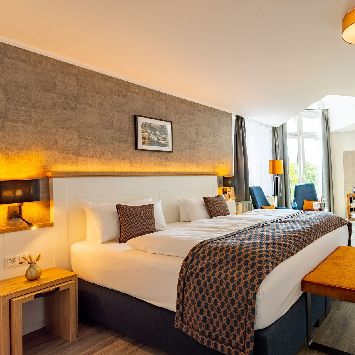 Hotelschlafzimmer mit großem Bett, Kunstwerken, Sitzbereich und Tageslicht.