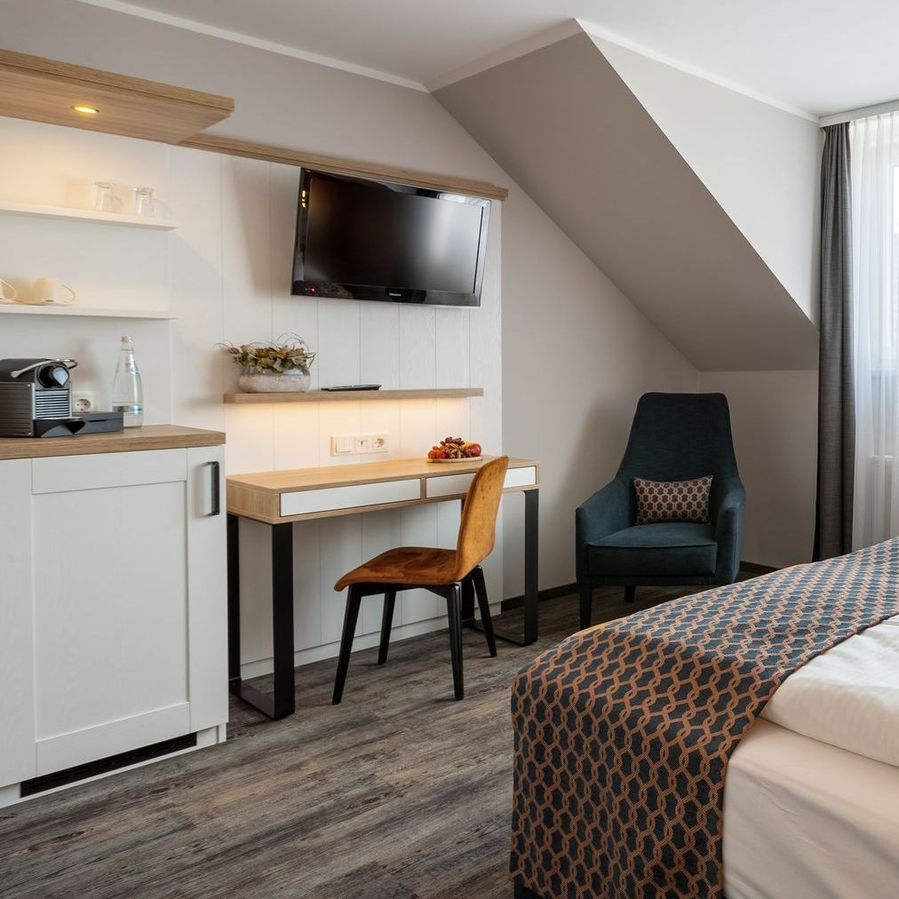 Hotelzimmer mit Bett, Schreibtisch, Stuhl, Fernseher, Küchenzeile und Sessel.