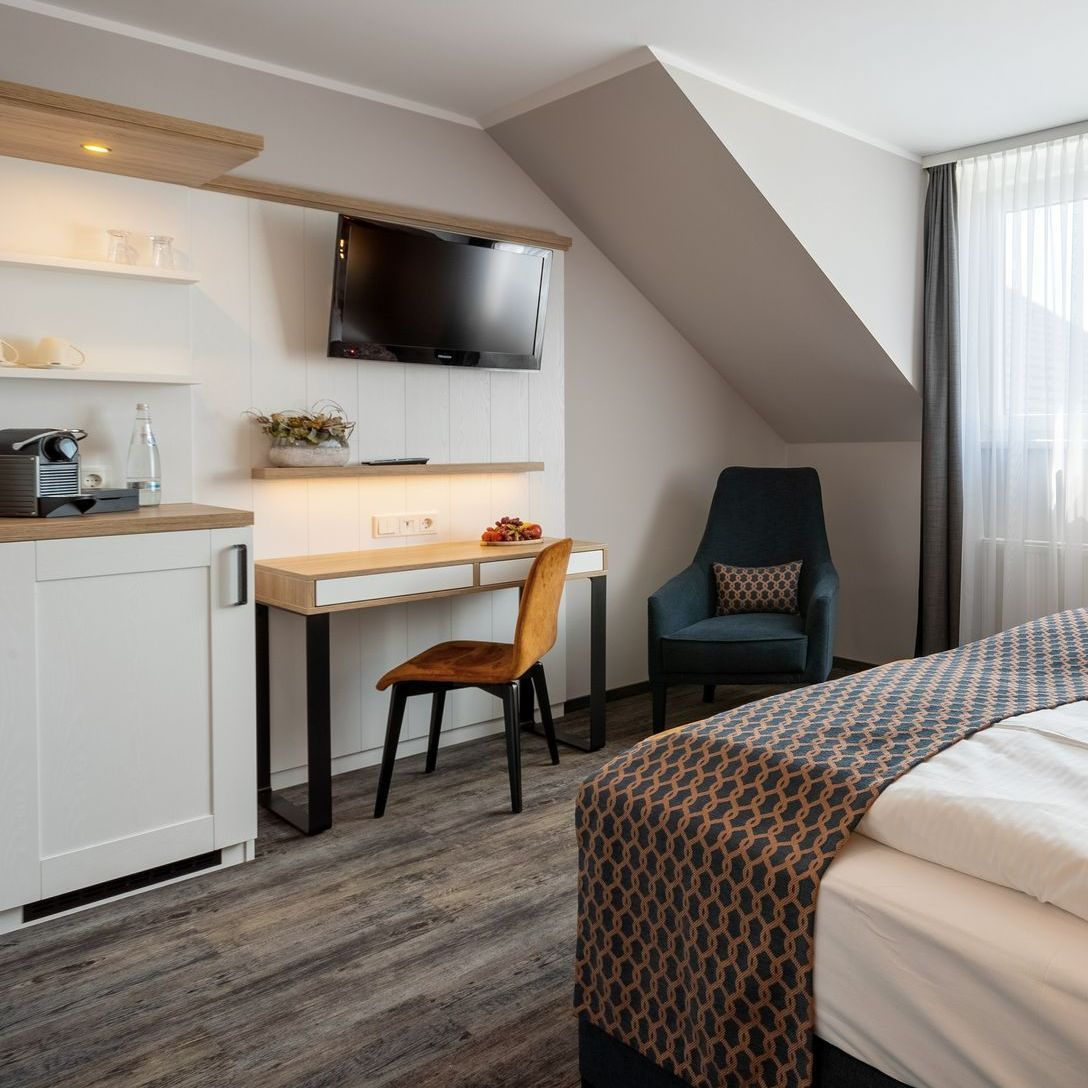 Hotelzimmer mit Bett, Schreibtisch, Stuhl, Sessel und einem an der Wand montierten Fernseher.