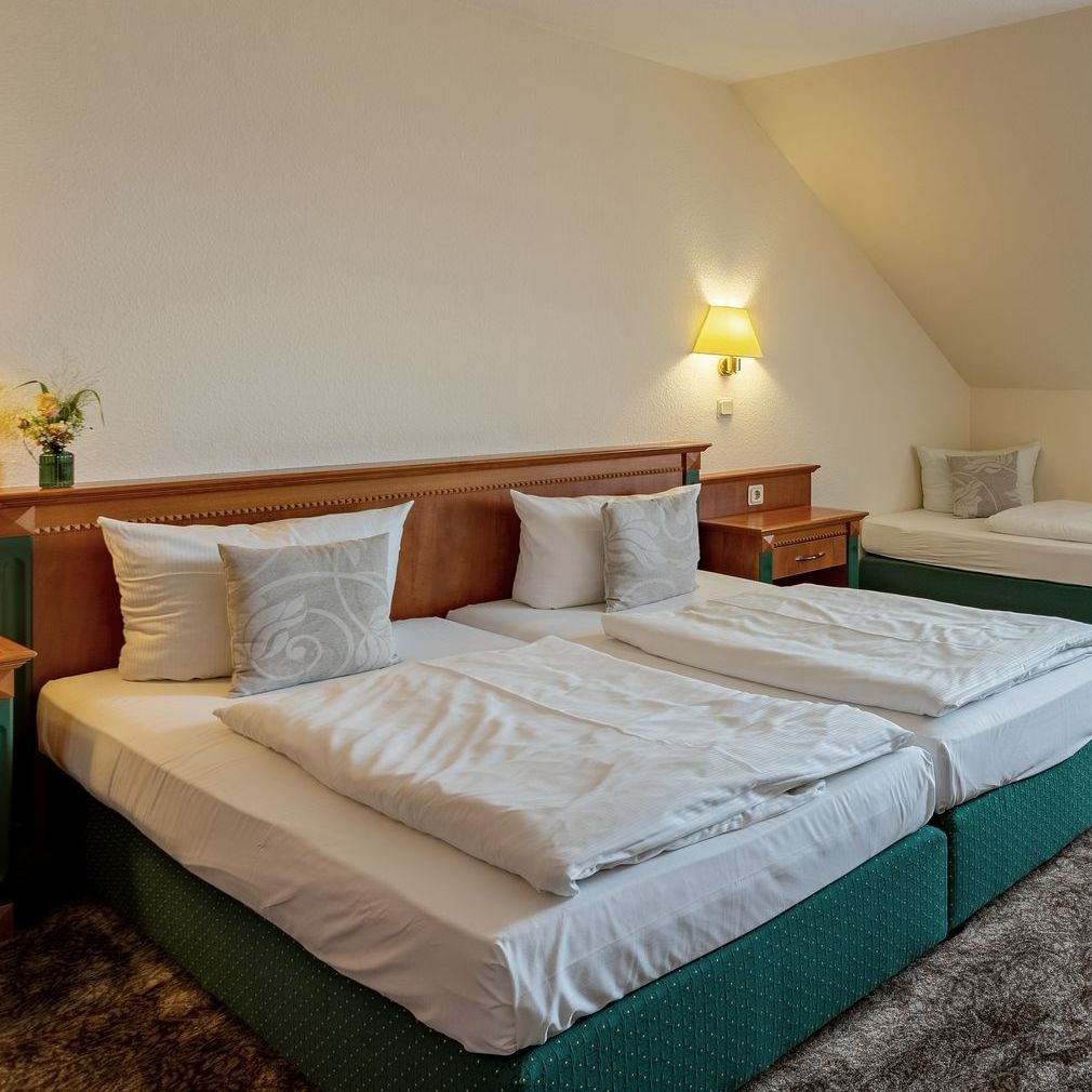 Hotelzimmer mit zwei Betten, weißer Bettwäsche und einem kleinen Bett im Hintergrund.