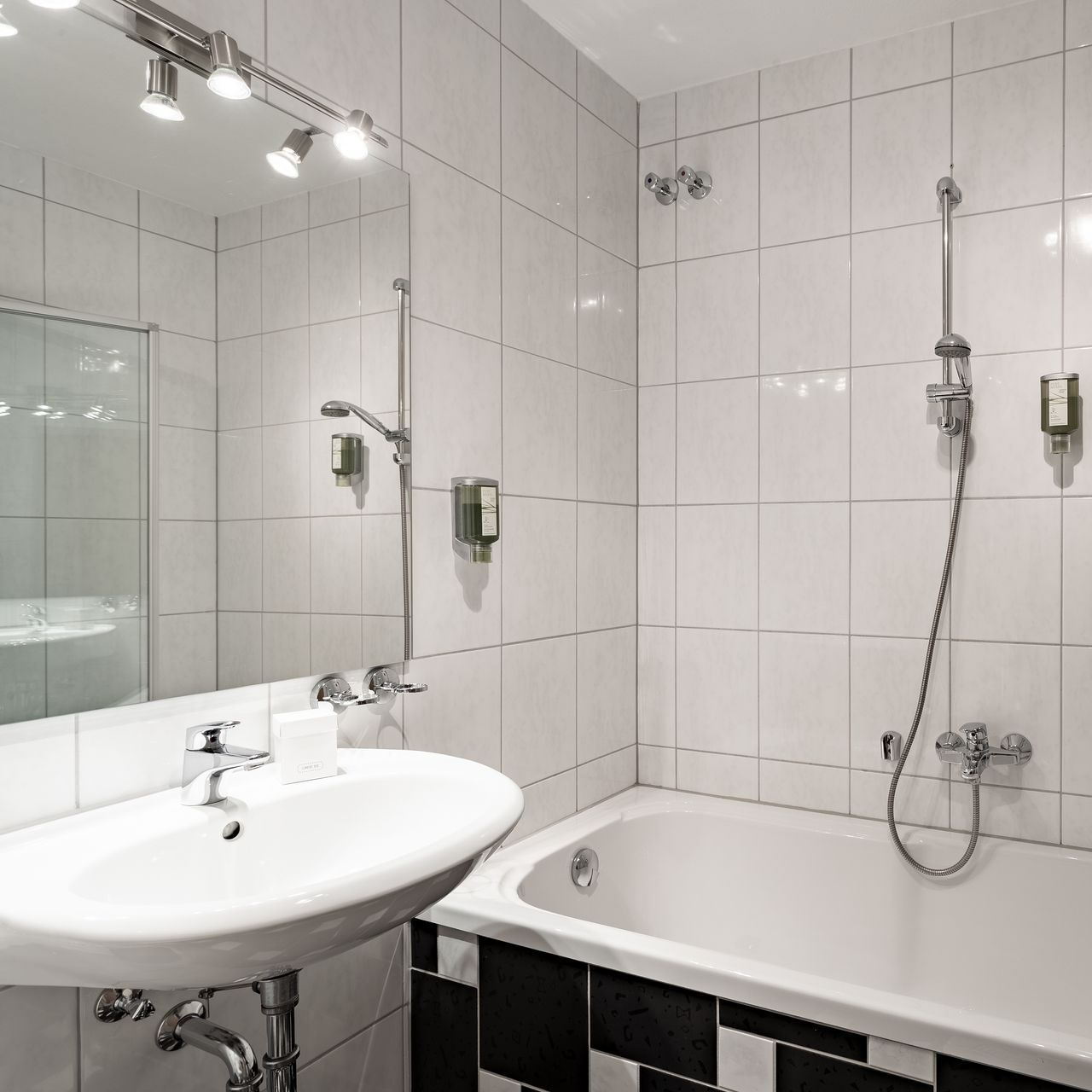 Ein Badezimmer mit weißem Waschbecken, Badewanne und gefliesten Wänden, schwarz-weißen Details.