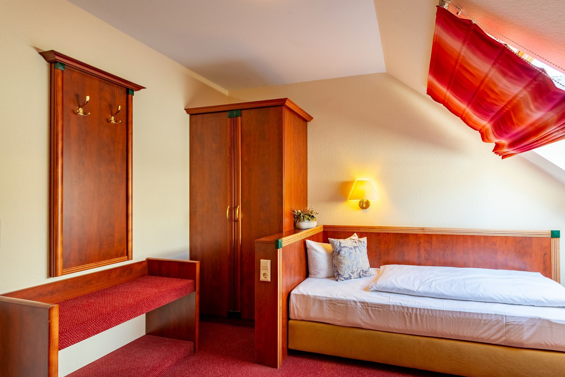 Schlafzimmer mit Bett, Kleiderschrank, Bank und roten Akzenten.