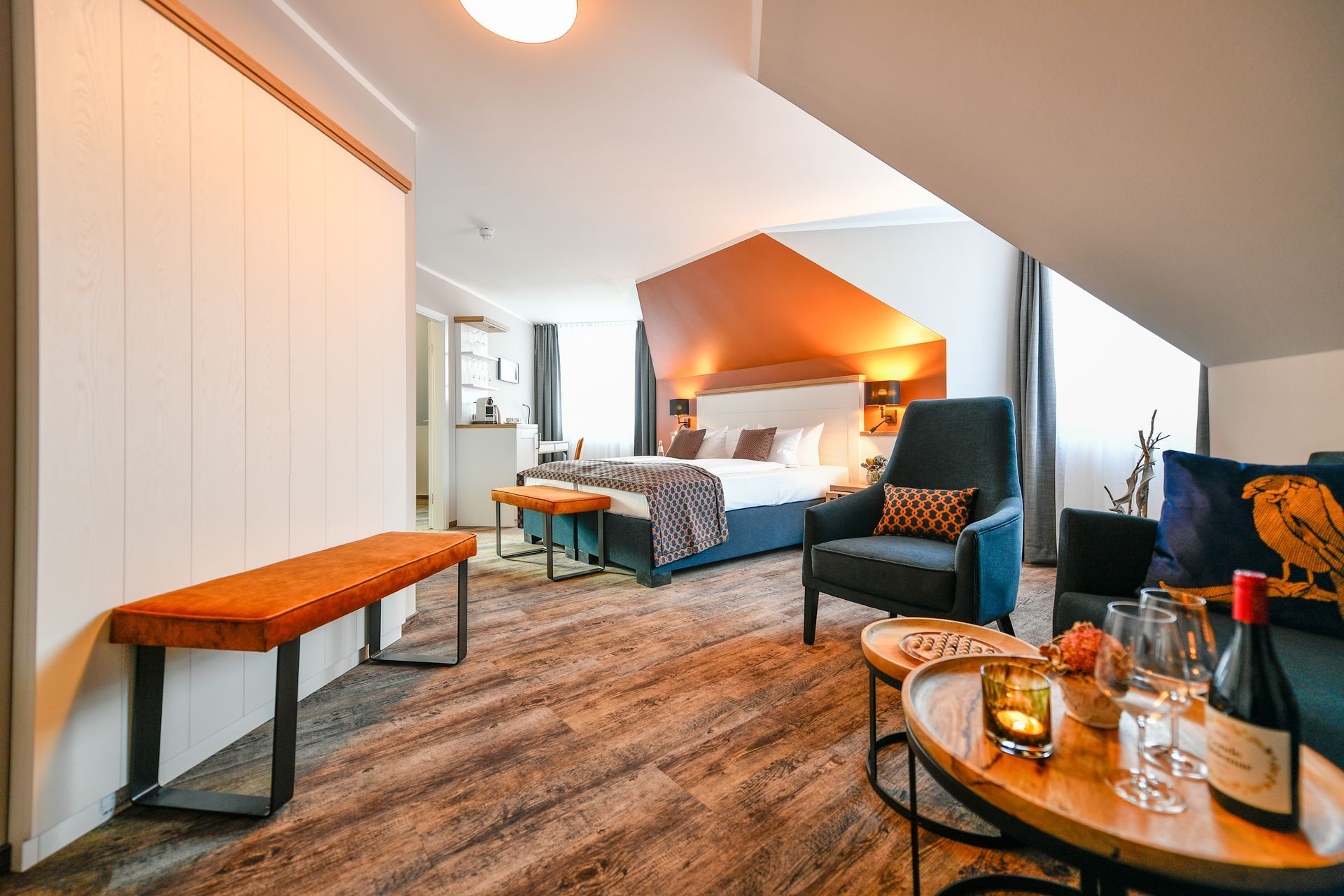 Hotelzimmer mit Bett, Sitzecke und orangefarbener Akzentwand.