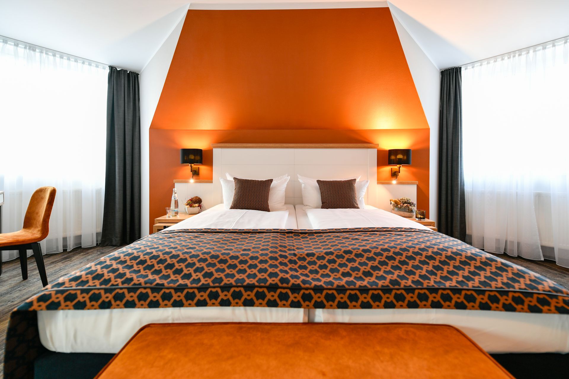 Hotelschlafzimmer mit Kingsize-Bett, orangefarbener Akzentwand und passender Bank.