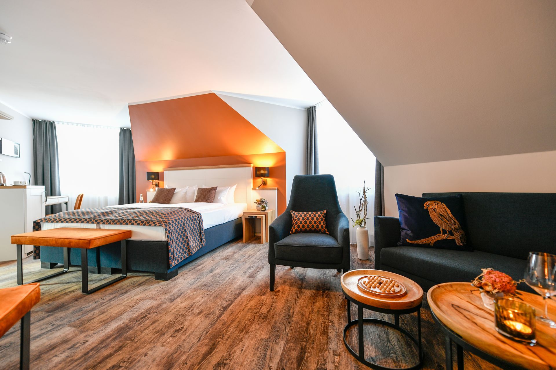 Hotelsuite mit Bett, Sofa, Sessel und kleinen Tischen. Dekor in Erdtönen mit Farbtupfern.