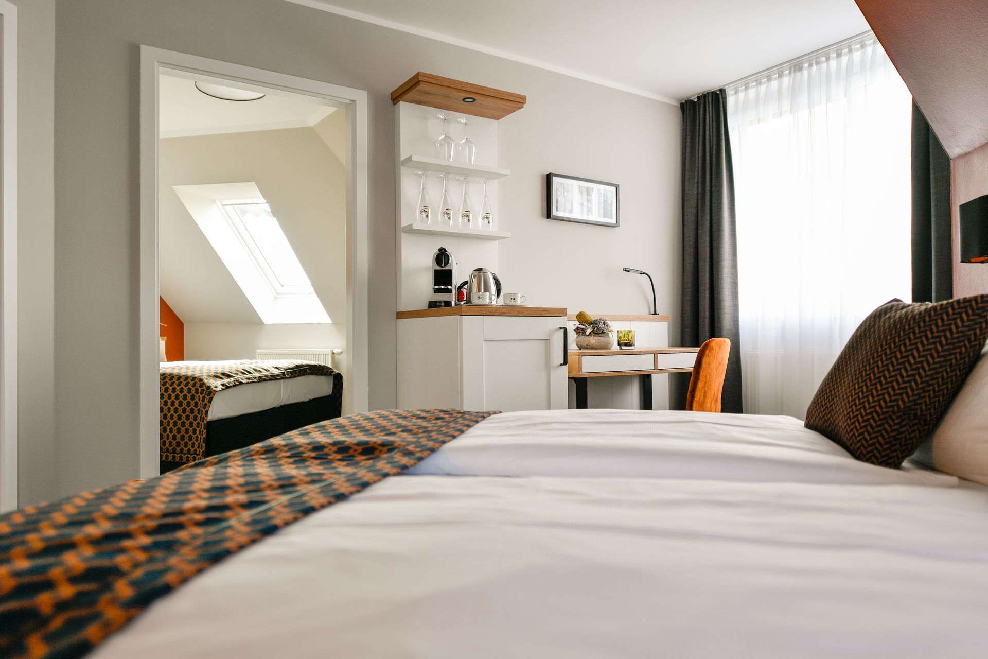 Schlafzimmer mit zwei Betten, Schreibtisch, Kaffeestation und Blick in ein weiteres Zimmer mit Bett und Dachfenster.