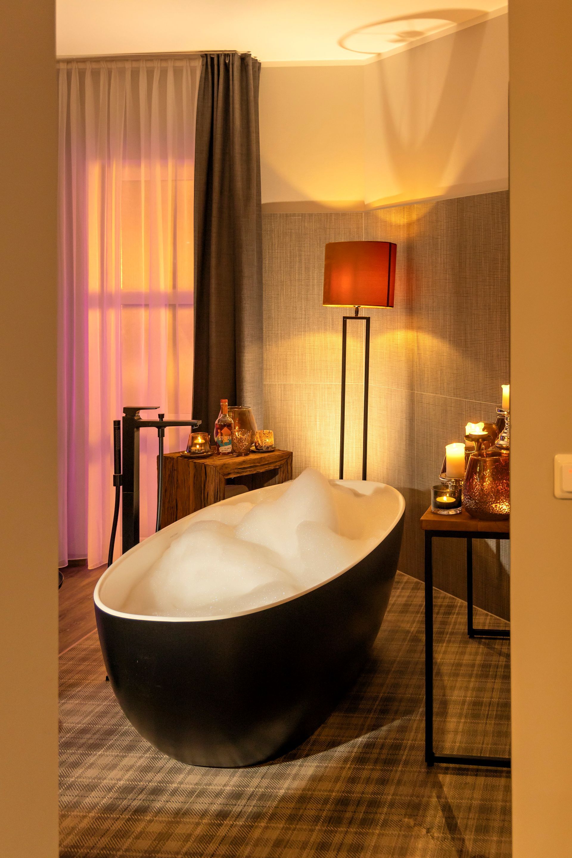 Schwarze Badewanne mit Schaum in einem gemütlichen Badezimmer mit warmer Beleuchtung.