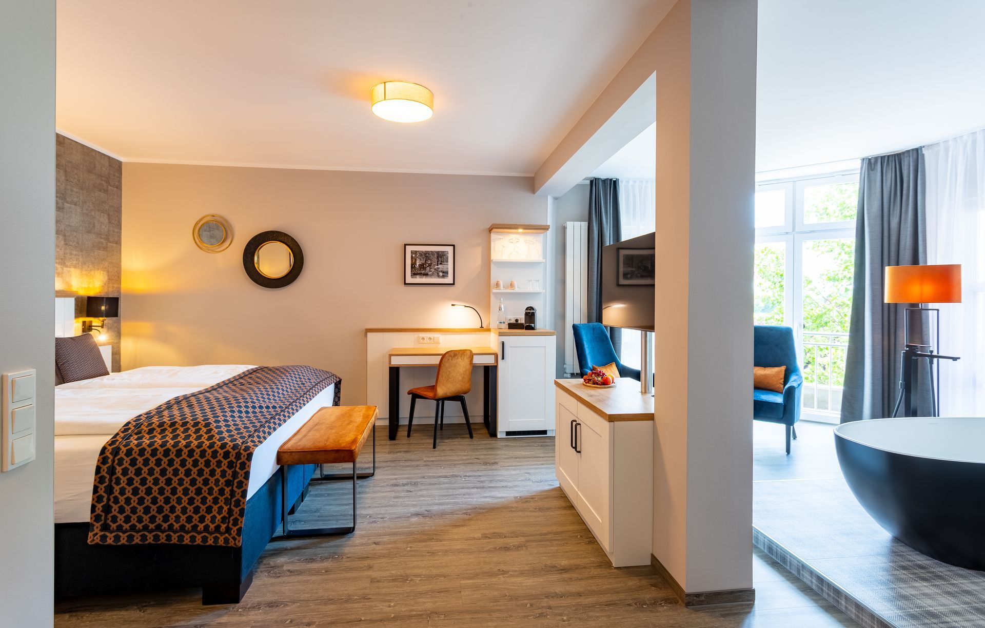 Hotelzimmer mit Bett, Schreibtisch, Sitzecke und freistehender Badewanne am Fenster.