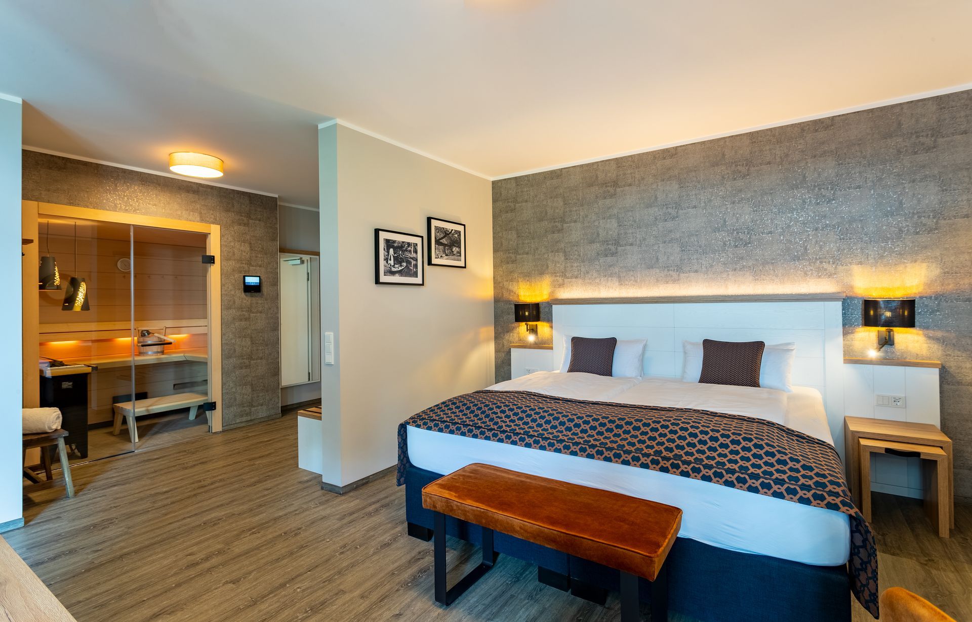 Hotelschlafzimmer mit Kingsize-Bett, Bank, Sauna und strukturierter grauer Wand.