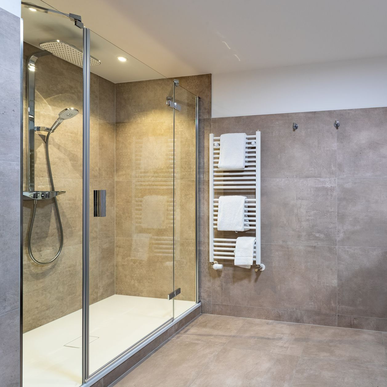 Modernes Badezimmer mit Glasdusche, Handtuchhalter und grau gefliesten Wänden.