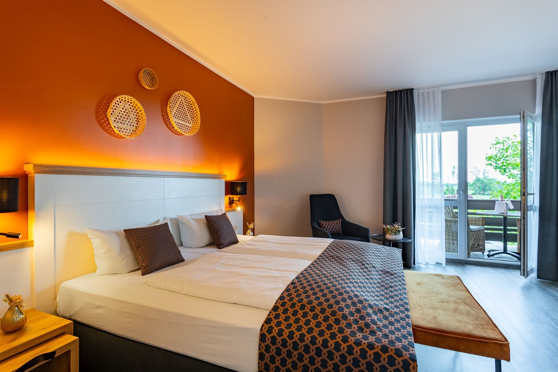 Hotelzimmer mit Kingsize-Bett, orangefarbener Akzentwand, Balkon und Dekor in neutralen Tönen.