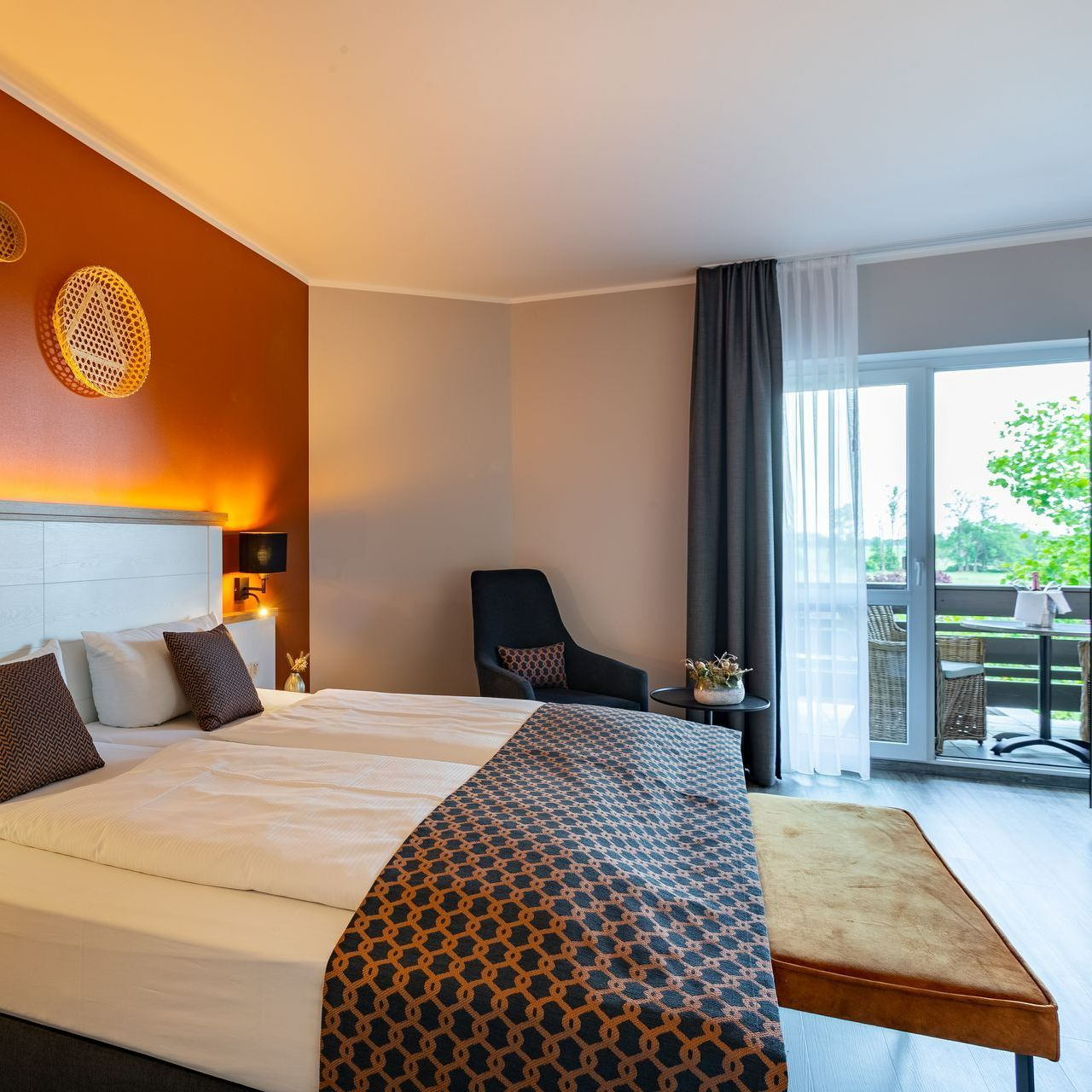 Hotelschlafzimmer mit Bett, Stuhl, Balkon. Braun-, Weiß- und Grautöne.