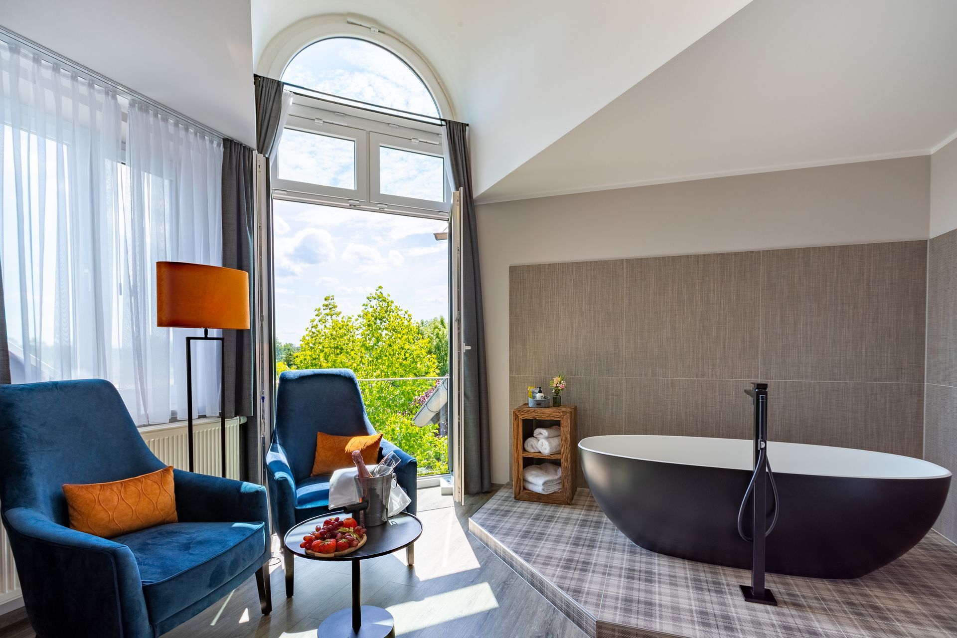 Badezimmer mit blauen Sesseln, einer schwarzen Badewanne und Blick auf grüne Bäume.