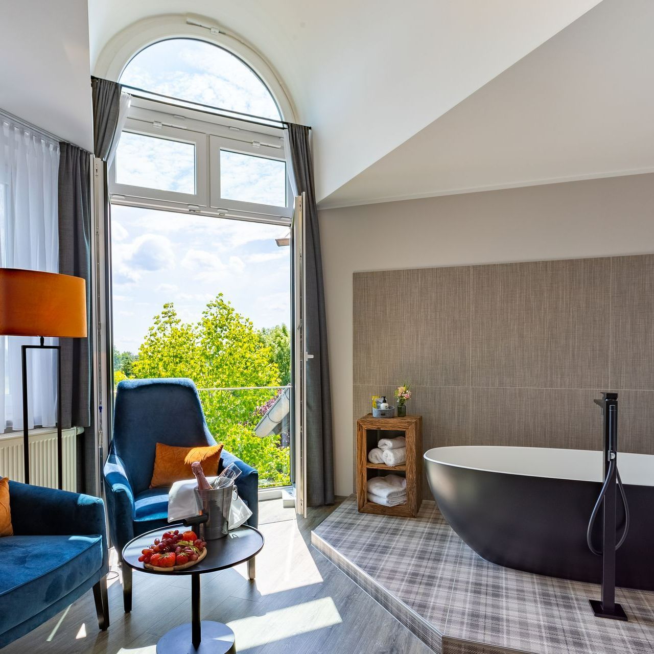 Luxuriöses Badezimmer mit schwarzer Badewanne, blauen Sitzgelegenheiten und einem Balkon mit Blick auf Bäume.