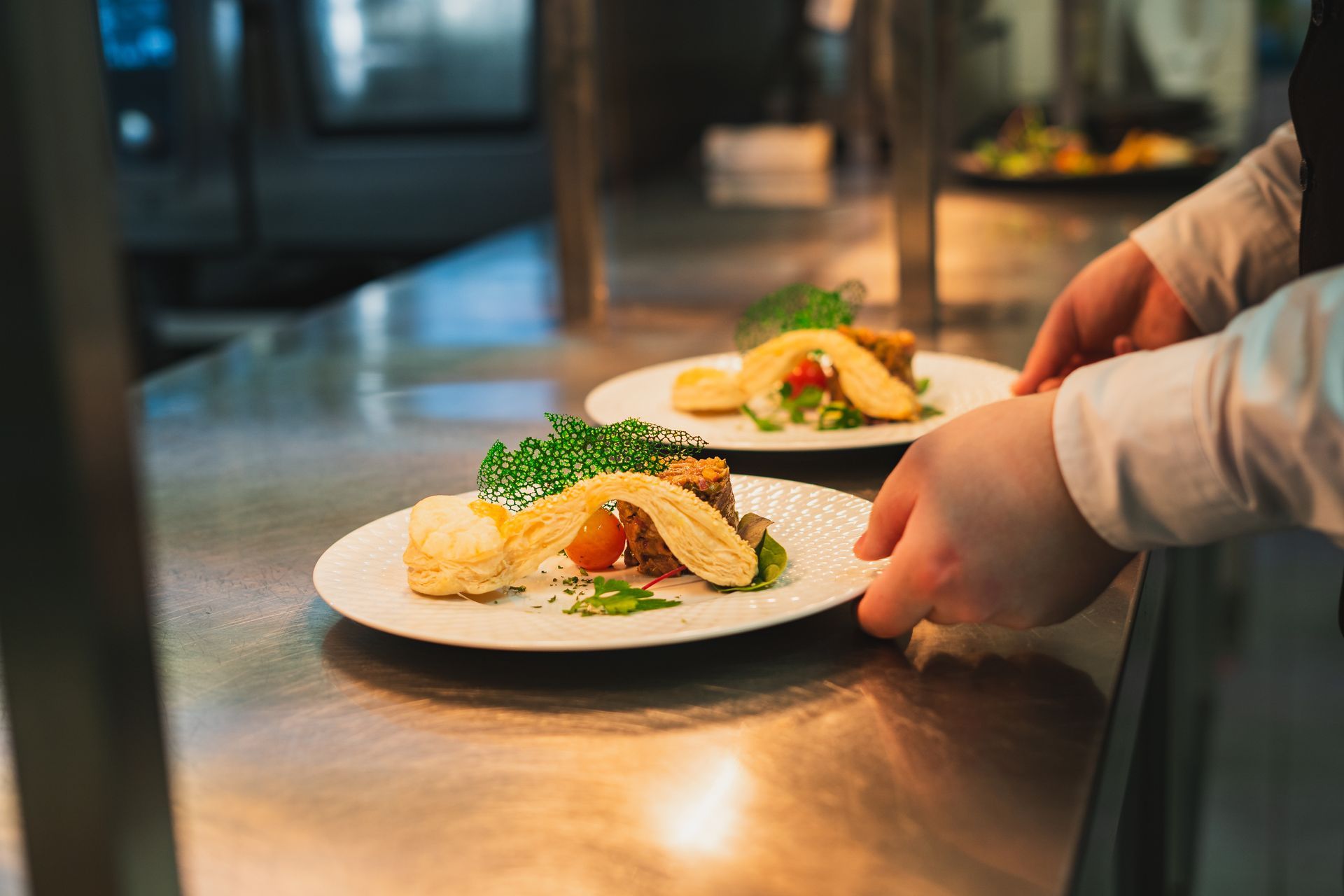 Zwei Teller mit Essen werden von einer Person in einer Restaurantküche gehalten.